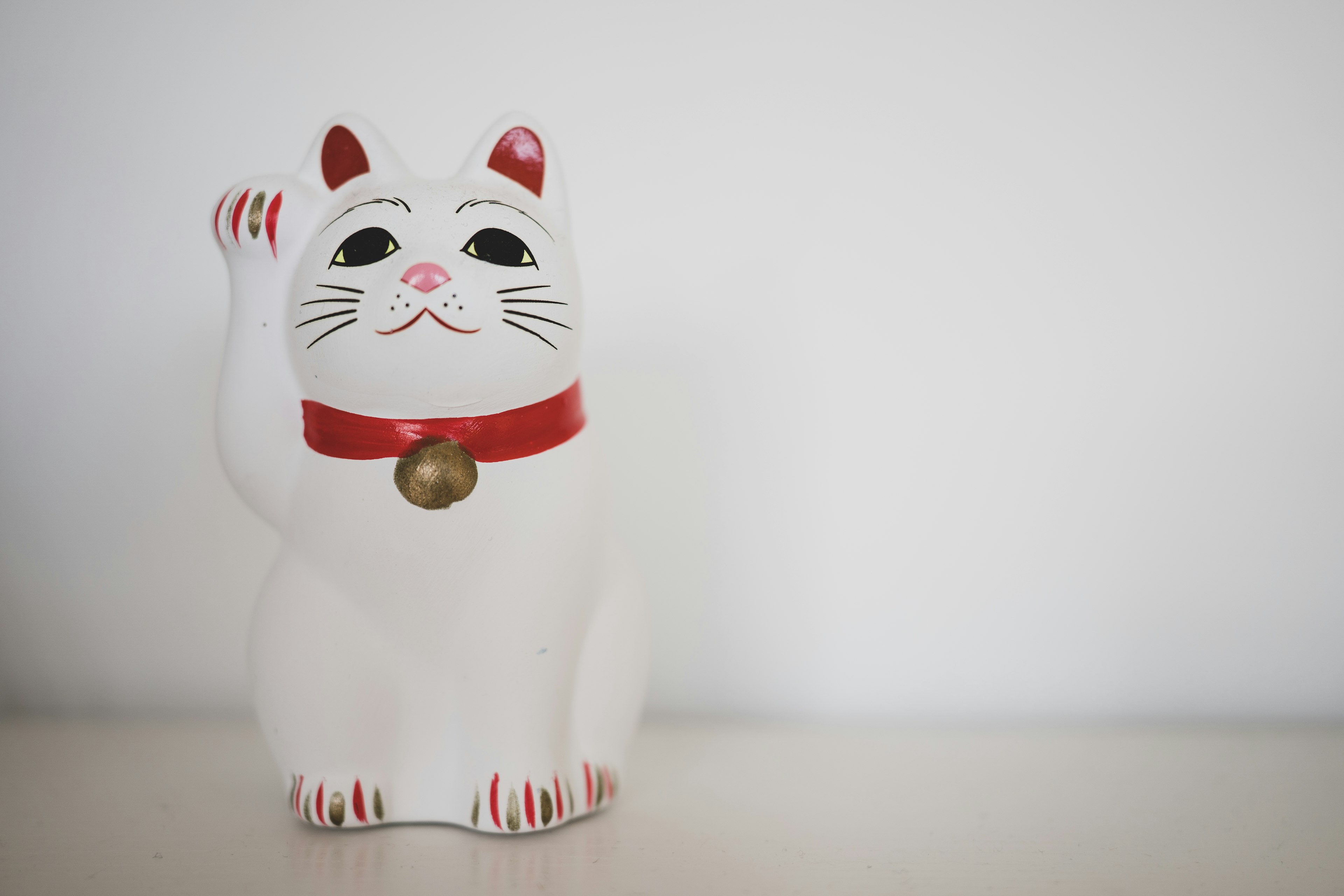 White lucky cat with a red collar and raised paw