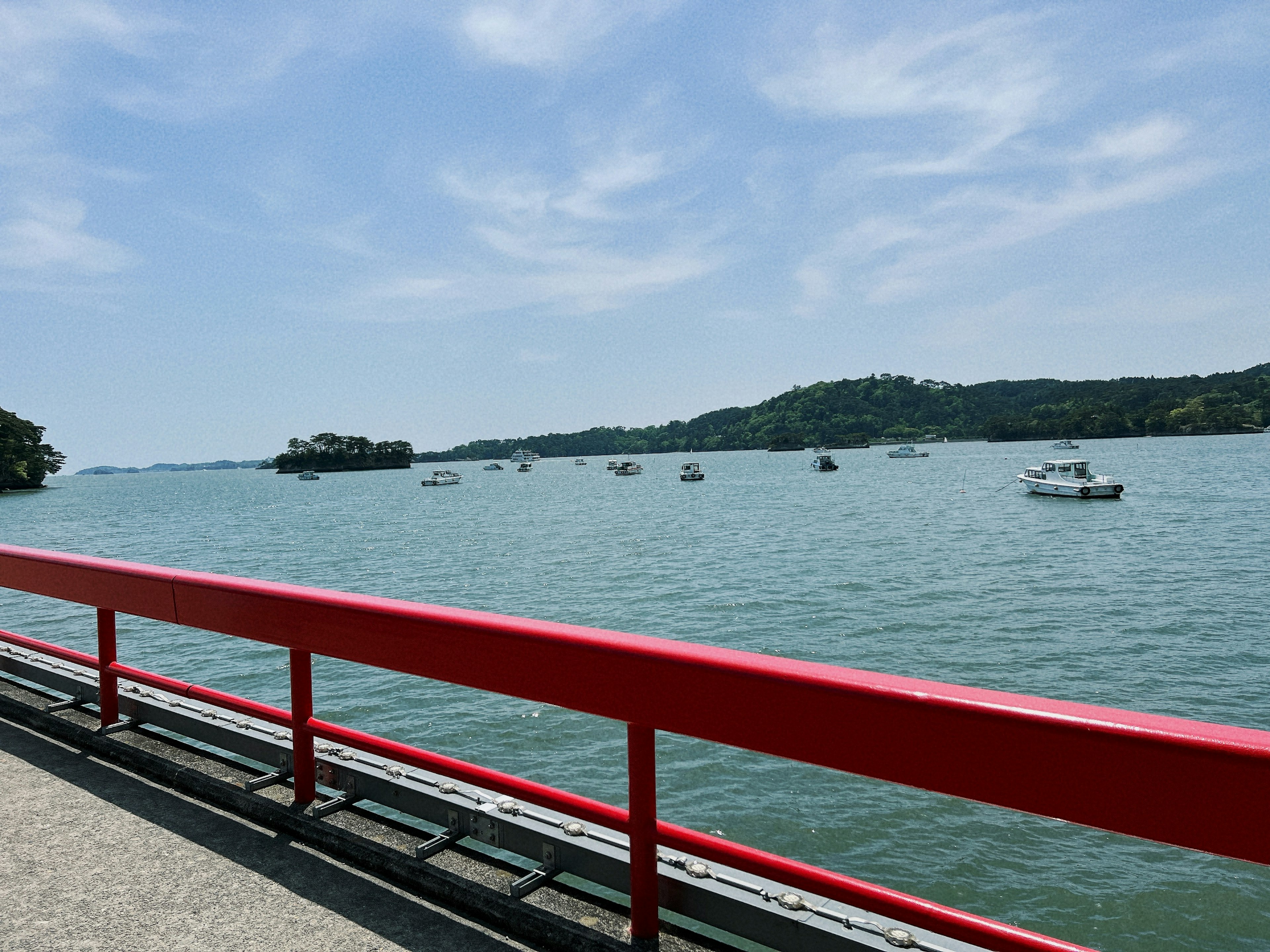 Coastal view with red railing small boats on calm water and blue sky