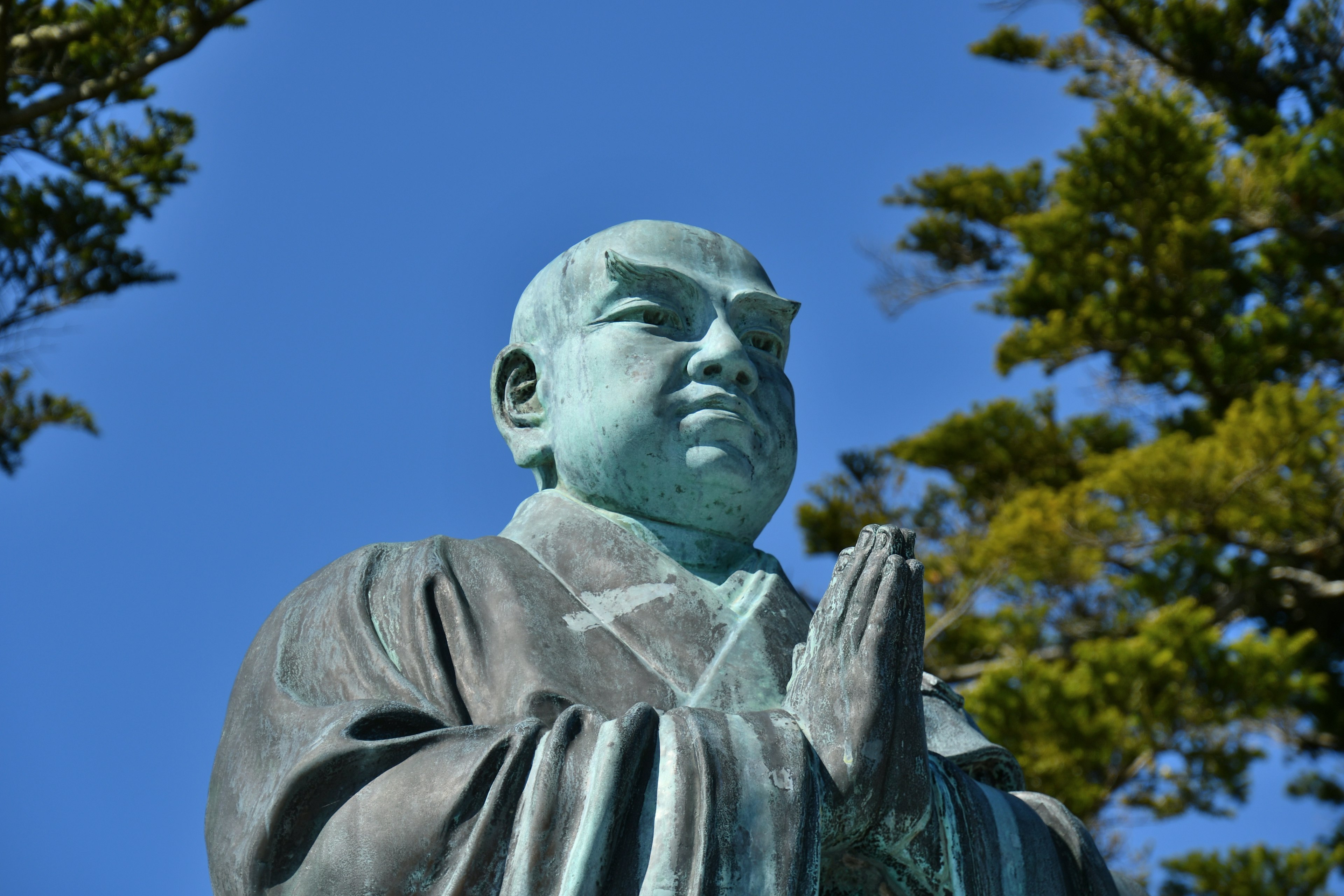 Buddha statue with hands in prayer under a blue sky