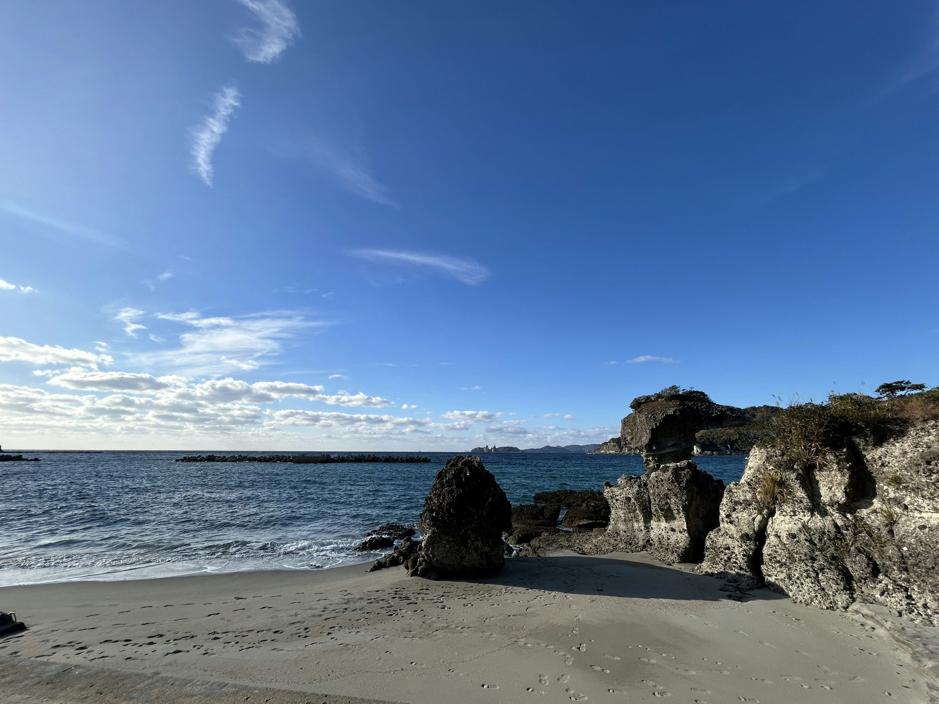 Malersicher Strandblick mit blauem Himmel und ruhigem Meer mit Felsen und Sandstrand