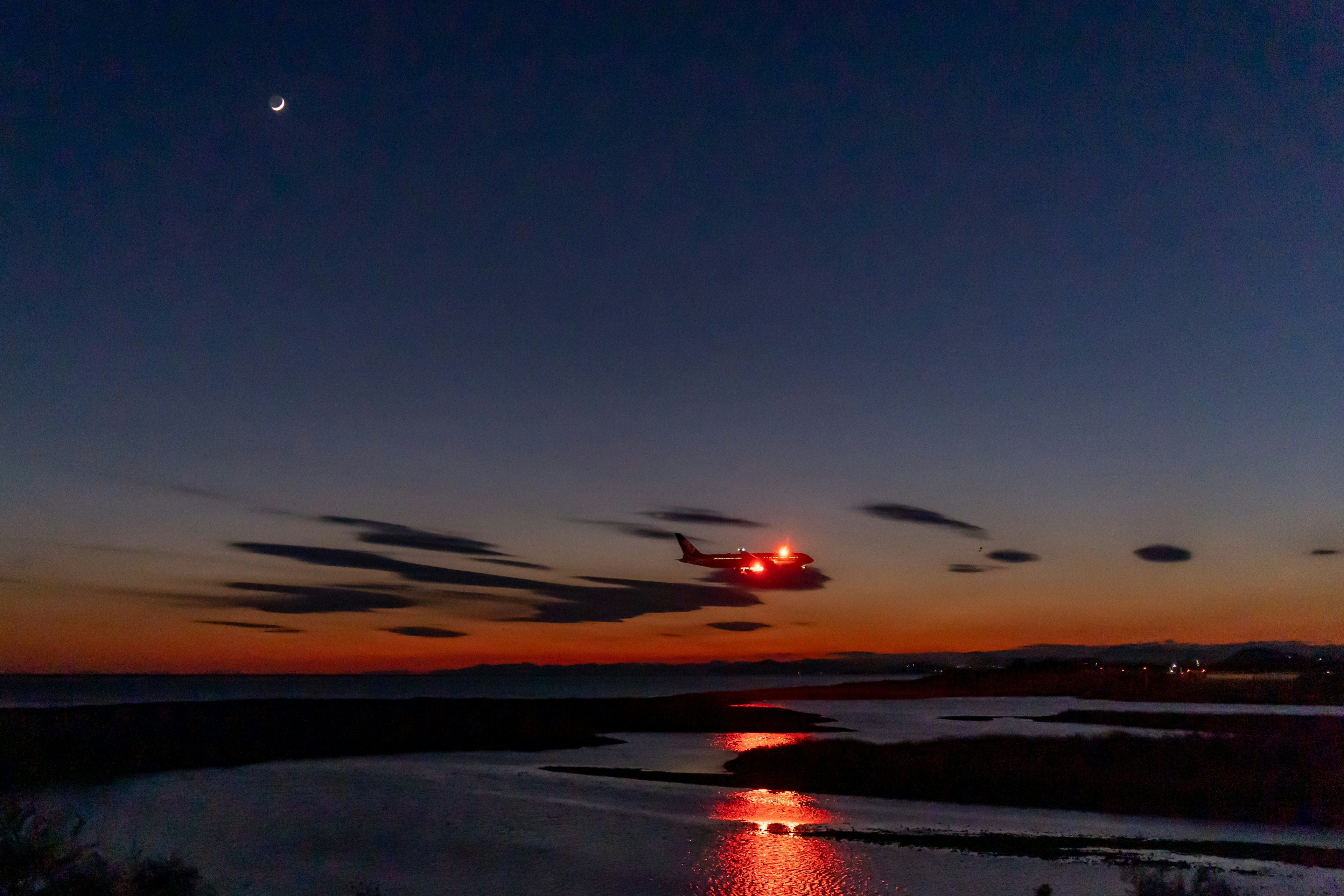 Hubschrauber fliegt gegen einen Dämmerungshimmel mit Reflexionen auf dem Wasser