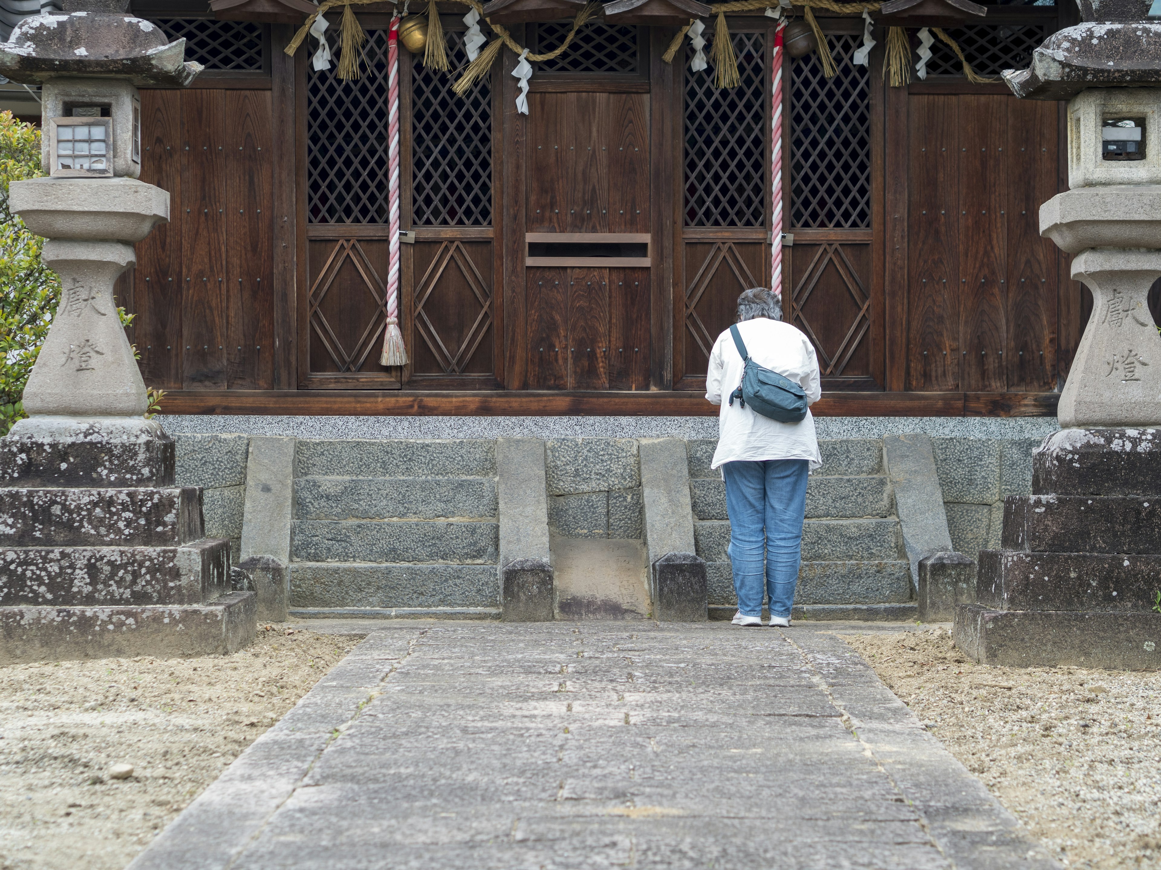 站在神社前的人穿着白色夹克和蓝色牛仔裤