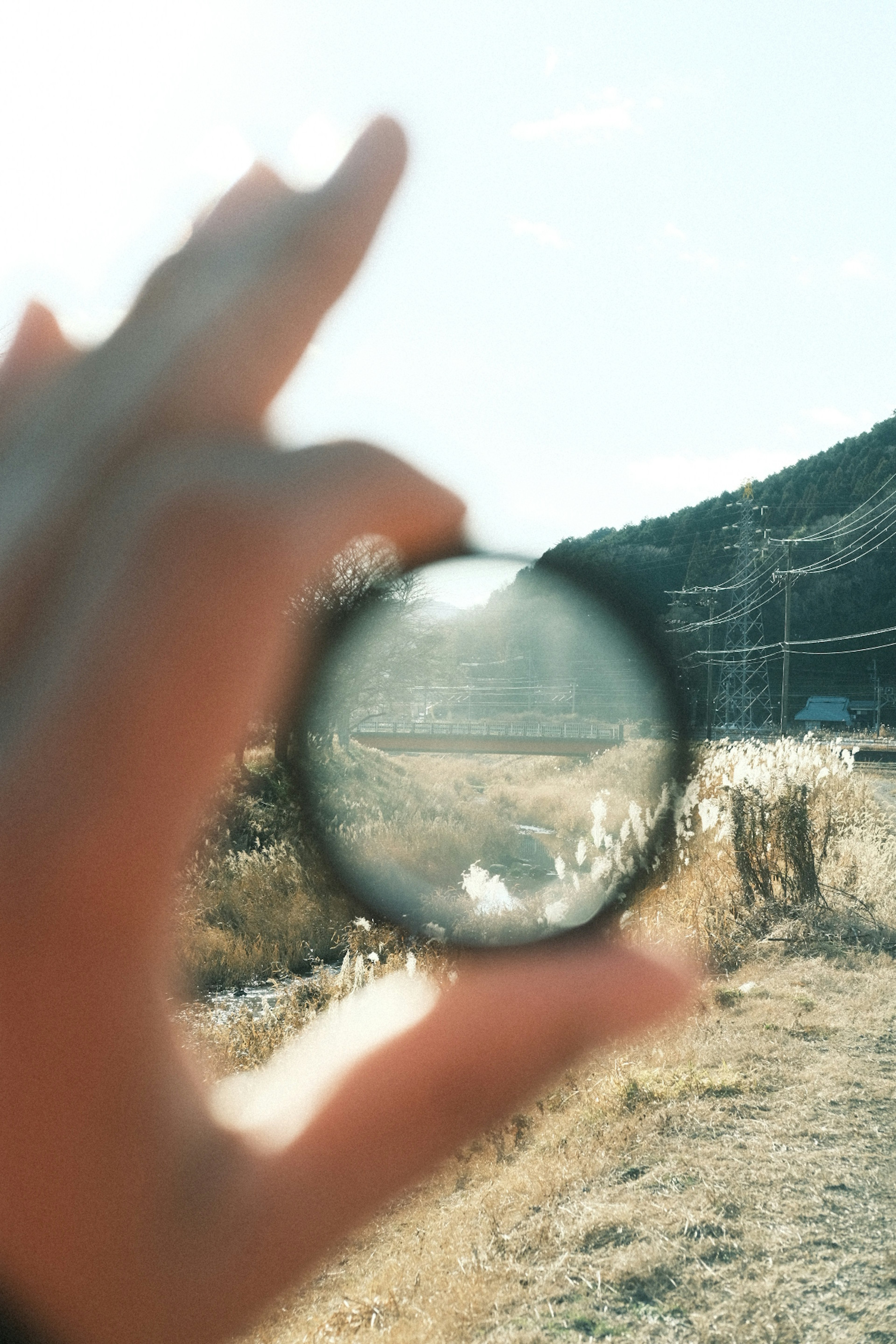 Una mano sosteniendo una lente que muestra un paisaje y el contorno de una montaña