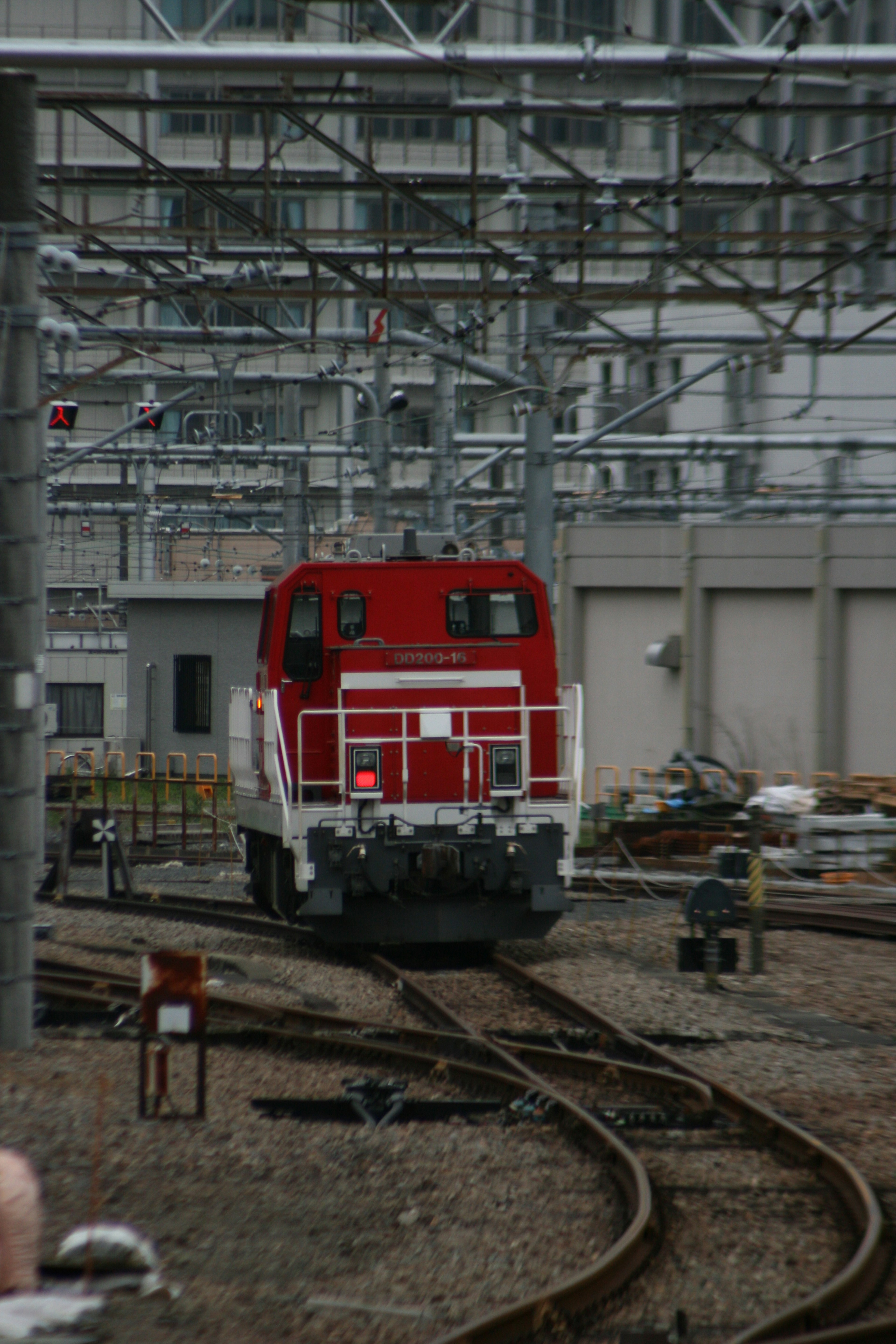 Red locomotive on railway tracks with industrial background