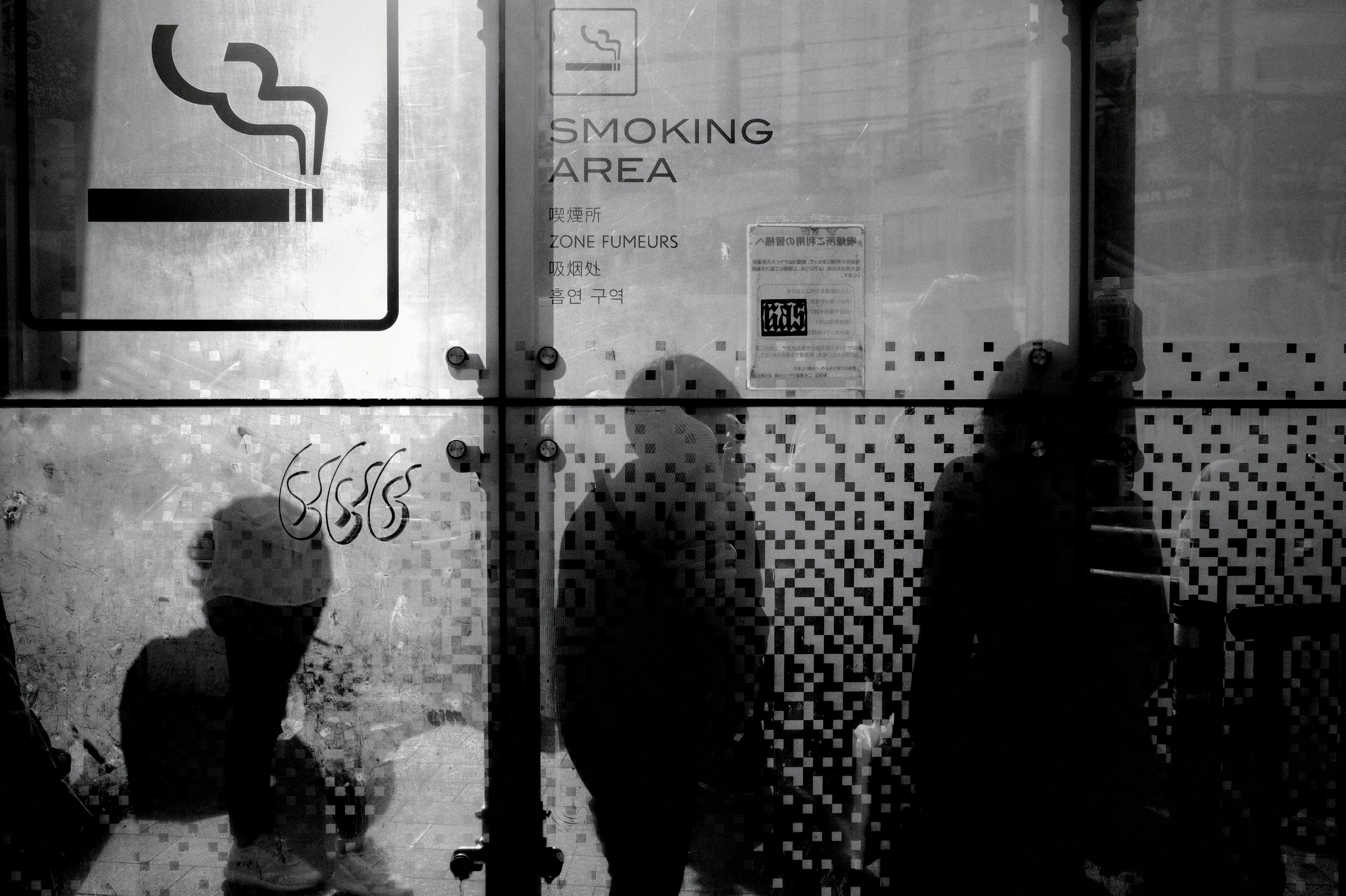 Silhouettes of people in front of a glass wall with a smoking area sign