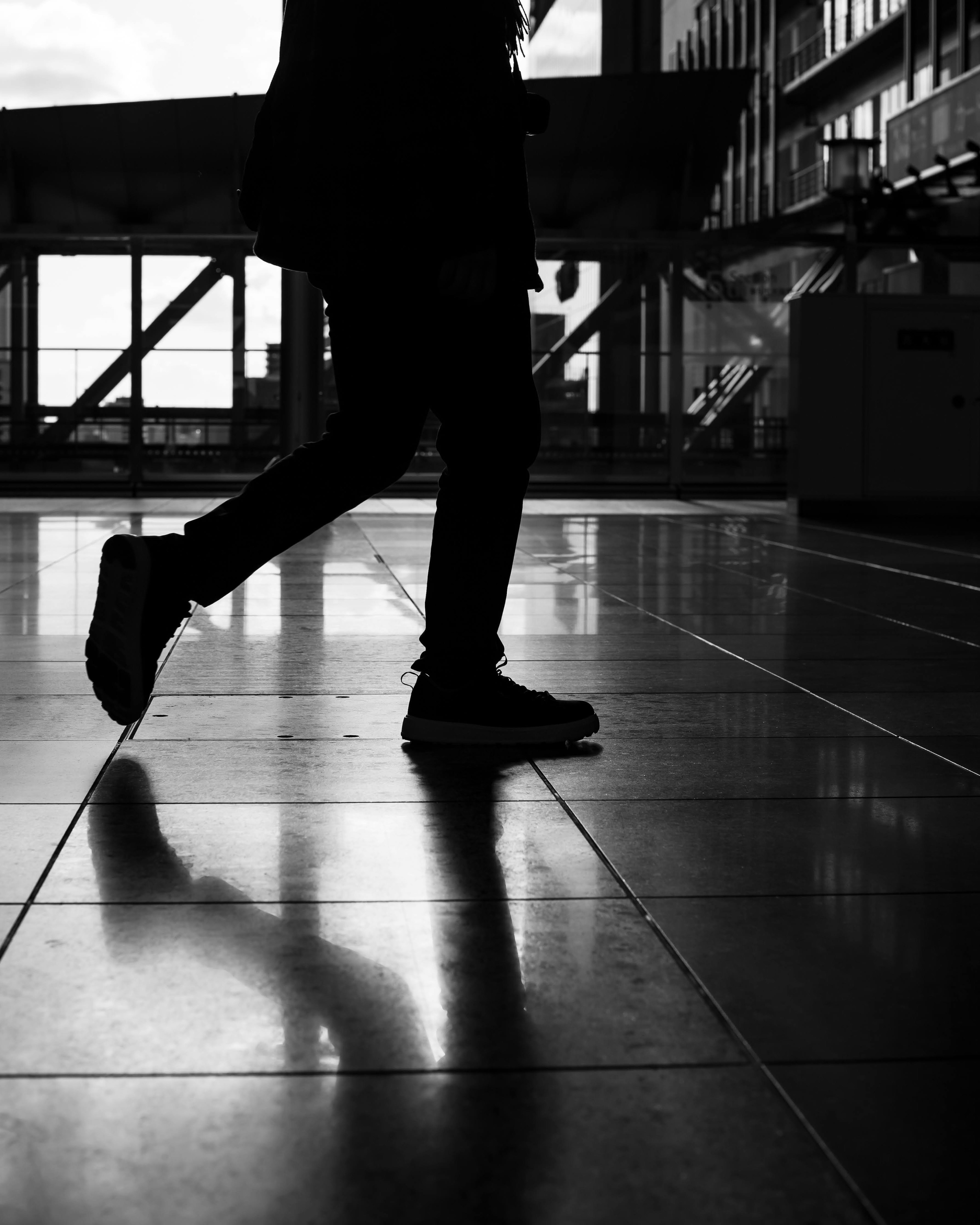 Silhouette of a person walking reflected on a shiny floor in black and white