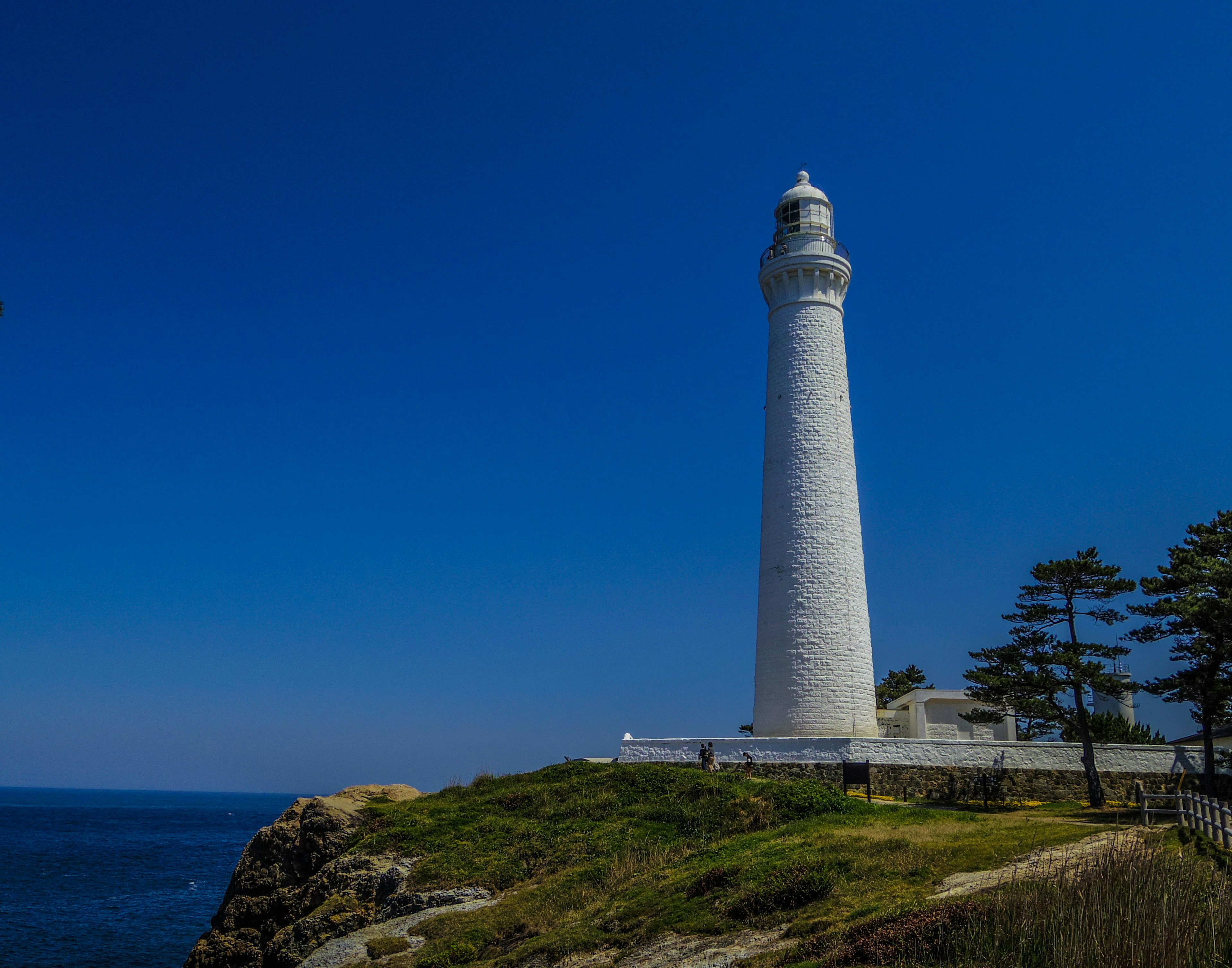 White lighthouse standing by the sea under a blue sky