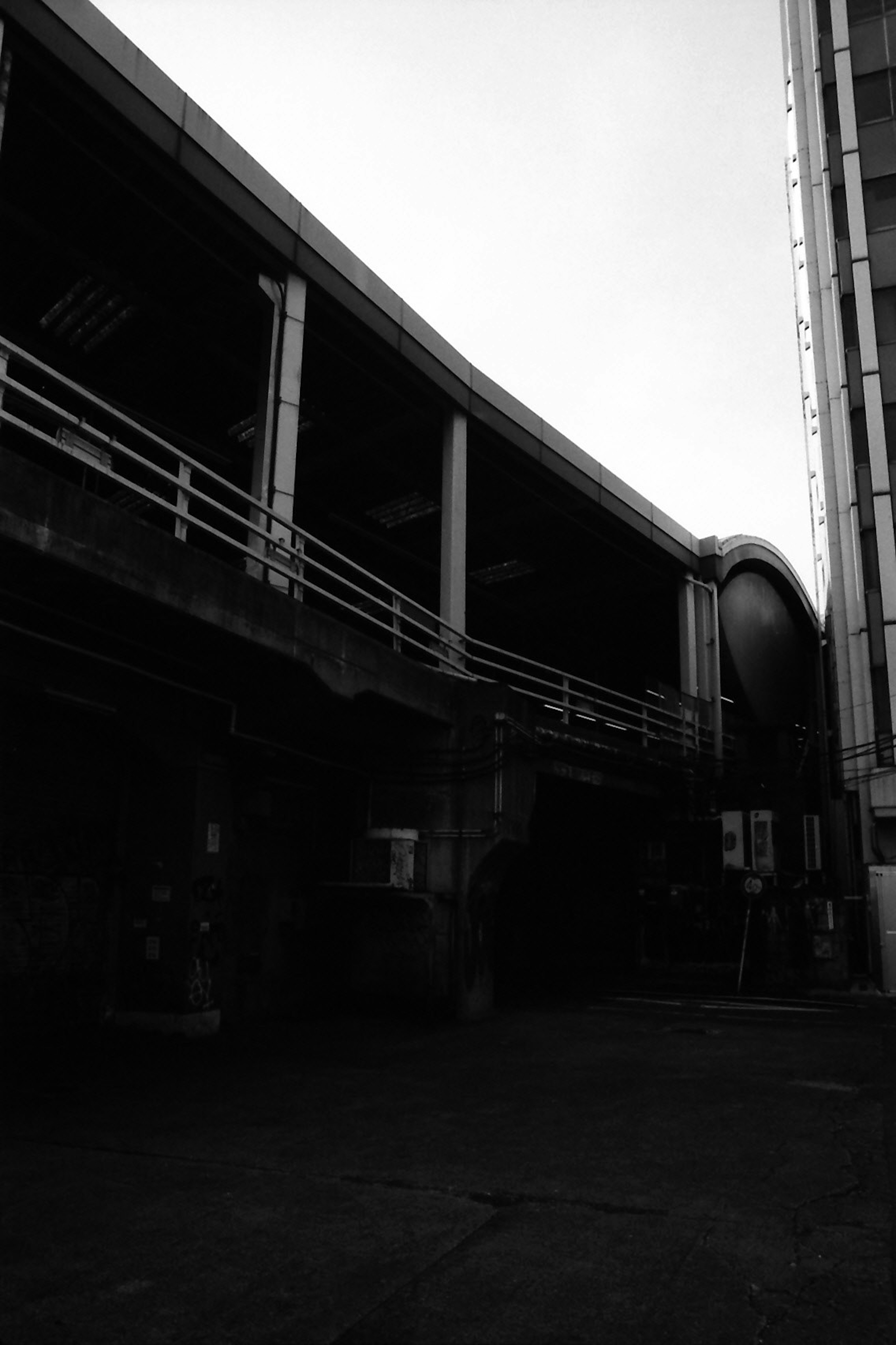 Black and white urban scene featuring a railway overpass and concrete building