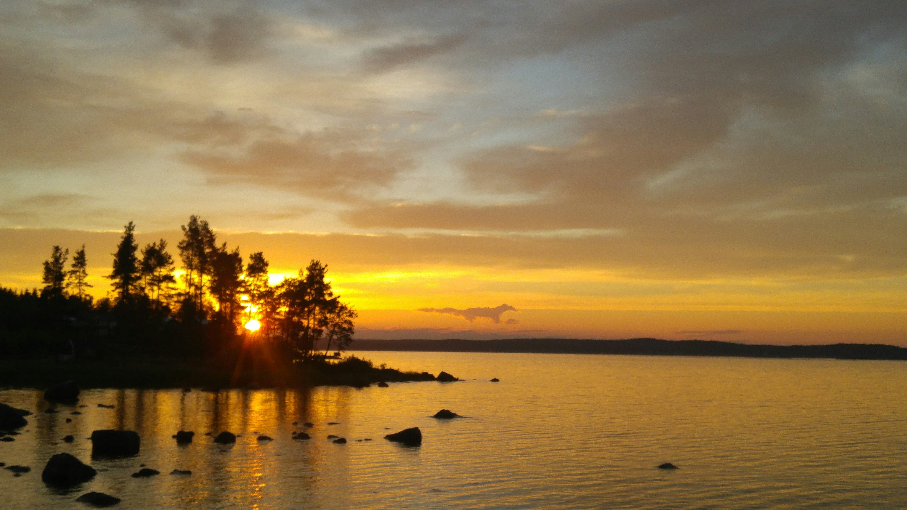 Malerscher Sonnenuntergang über einem See mit Silhouetten von Bäumen und Steinen