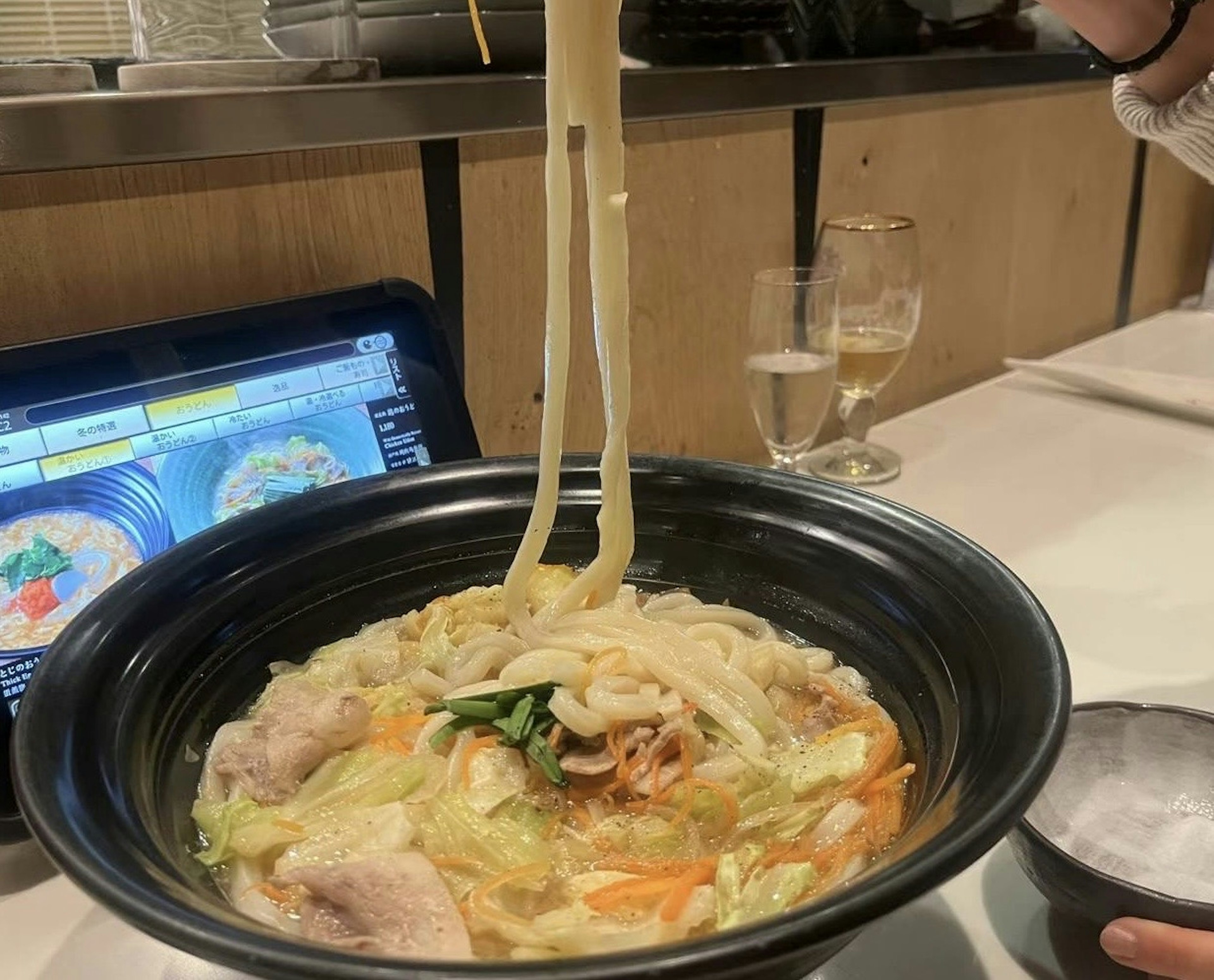 Mano levantando fideos udon de un tazón con verduras y caldo