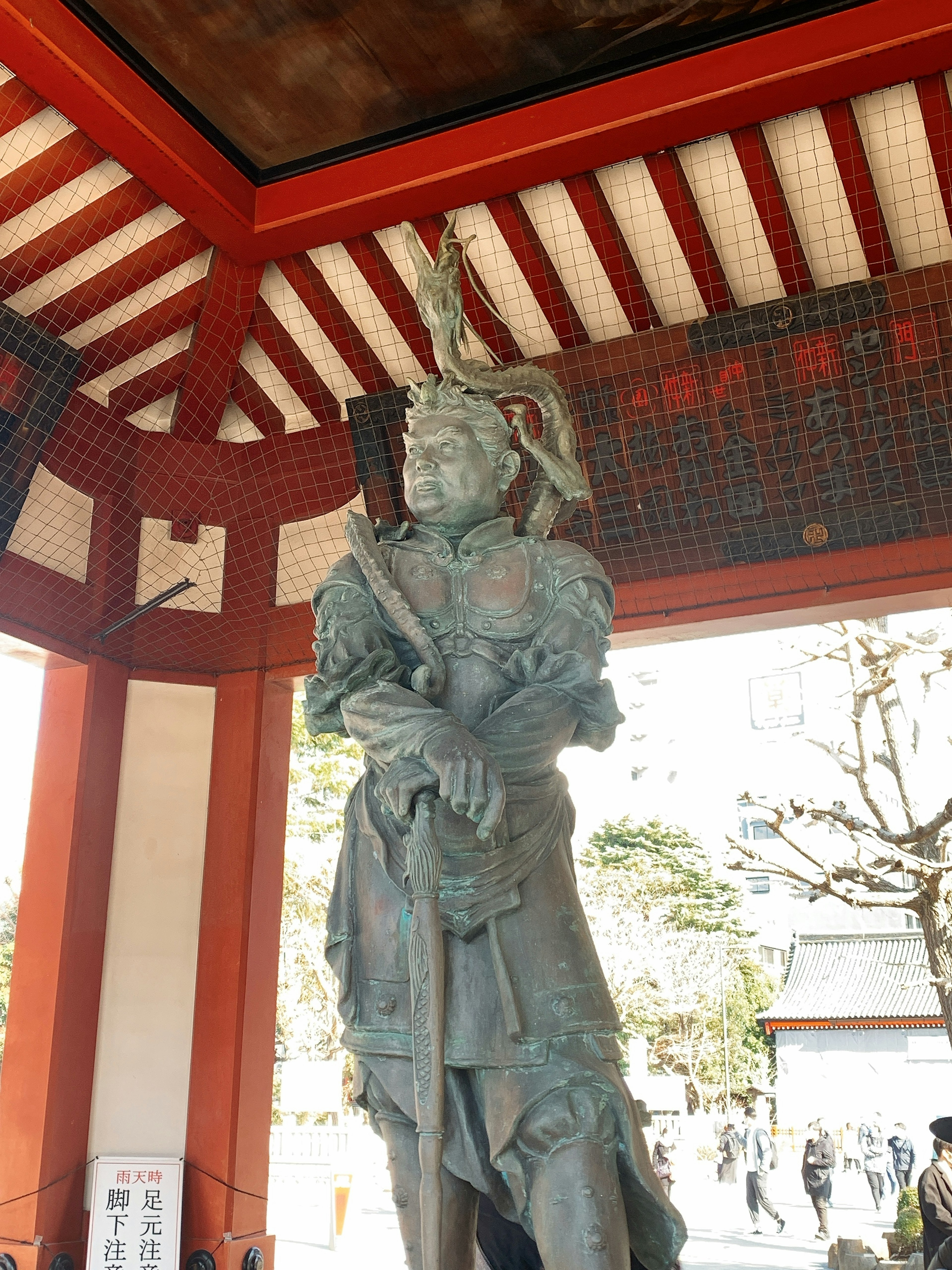 Bronze statue standing under a red-roofed structure