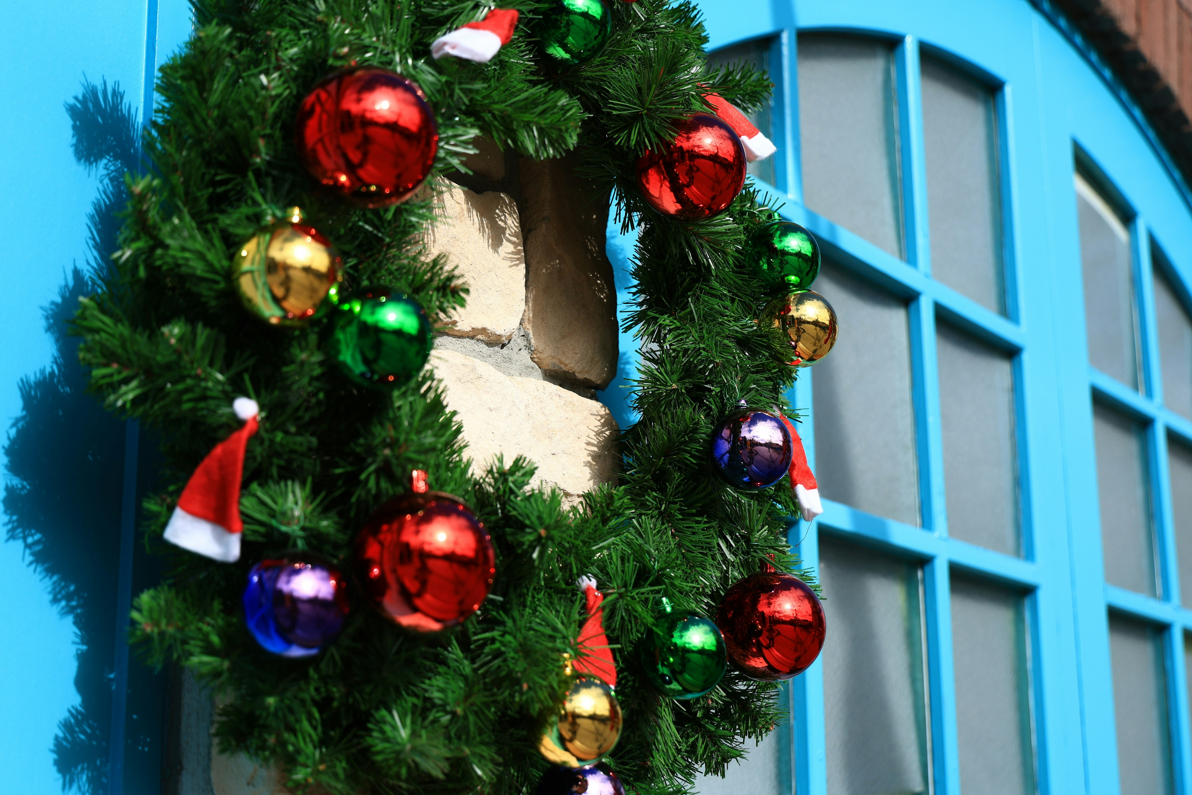 Christmas wreath adorned with red and green decorations and Santa hats on a blue door