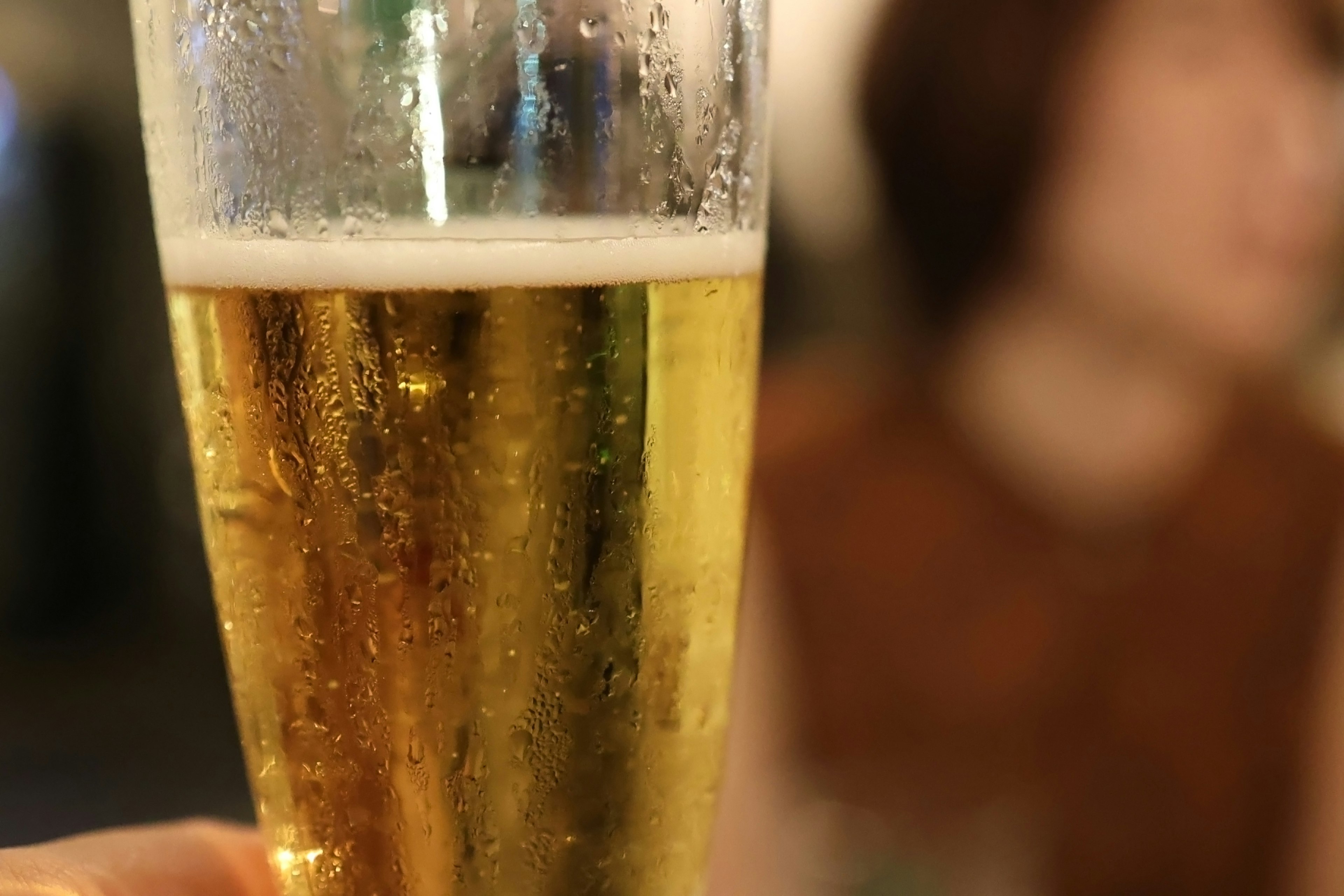 A close-up of a hand holding a chilled glass of beer