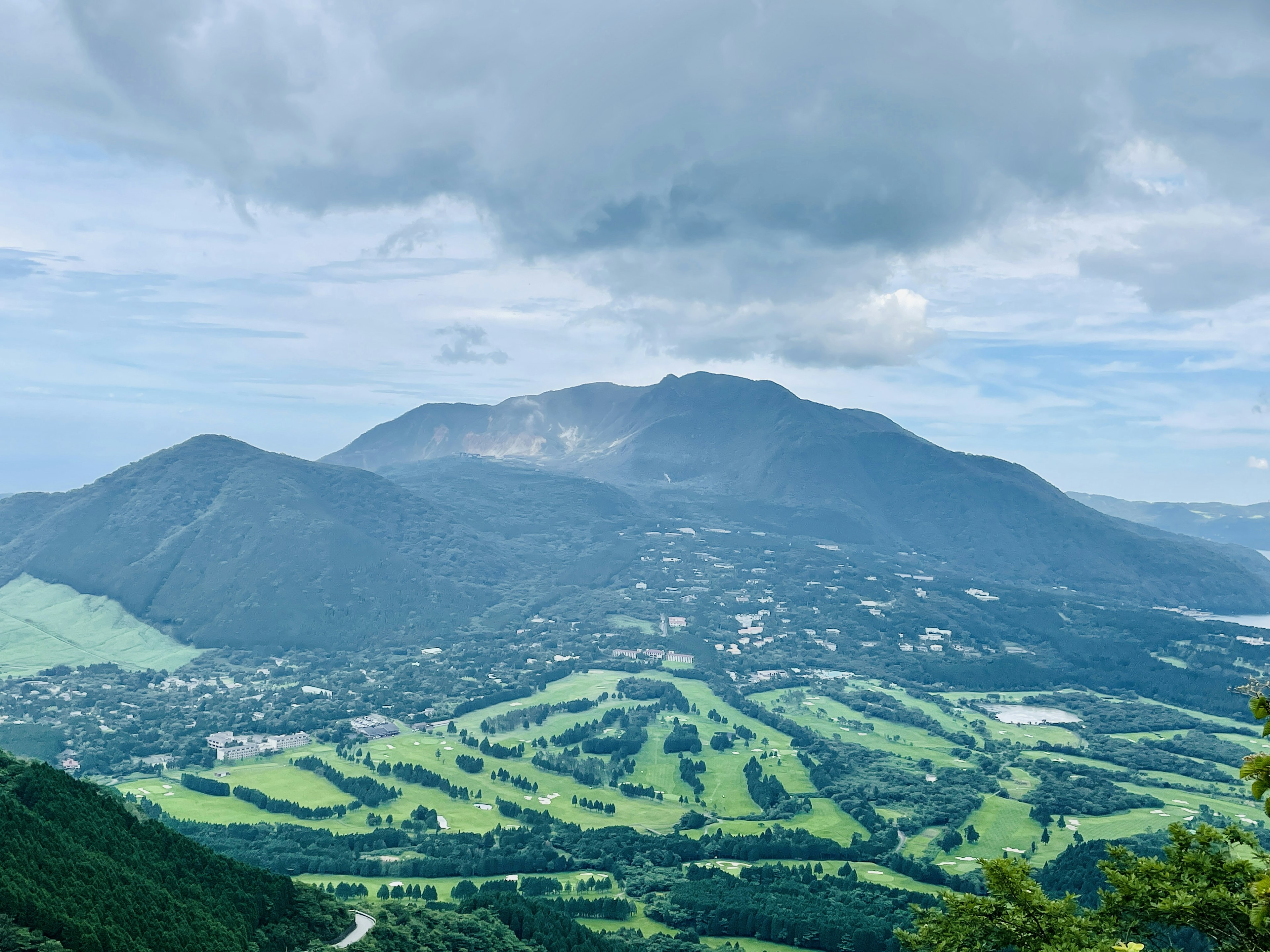 緑豊かな丘陵と雲に覆われた山々の景色