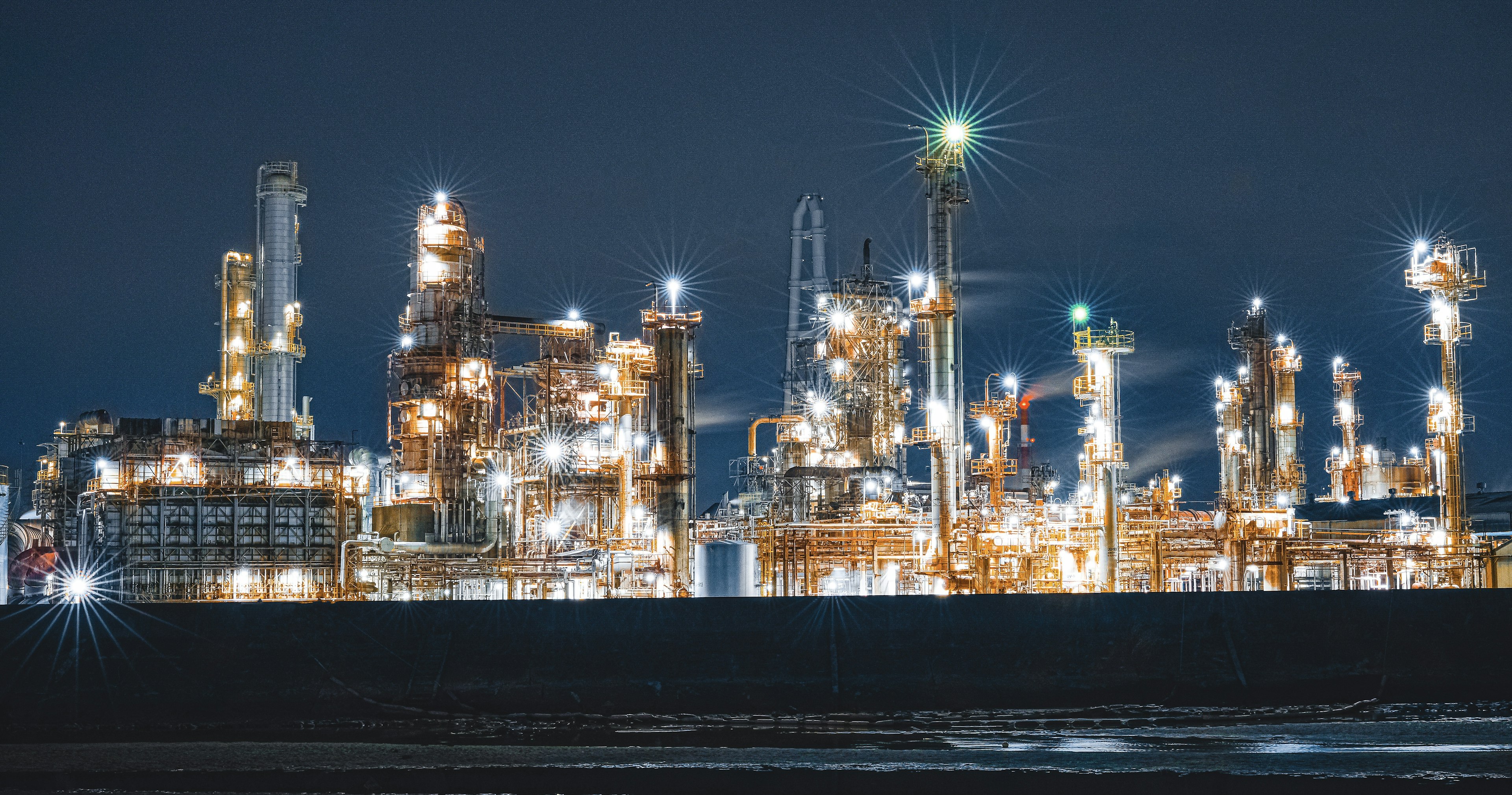 Illuminated industrial plant at night with glowing lights and smokestacks