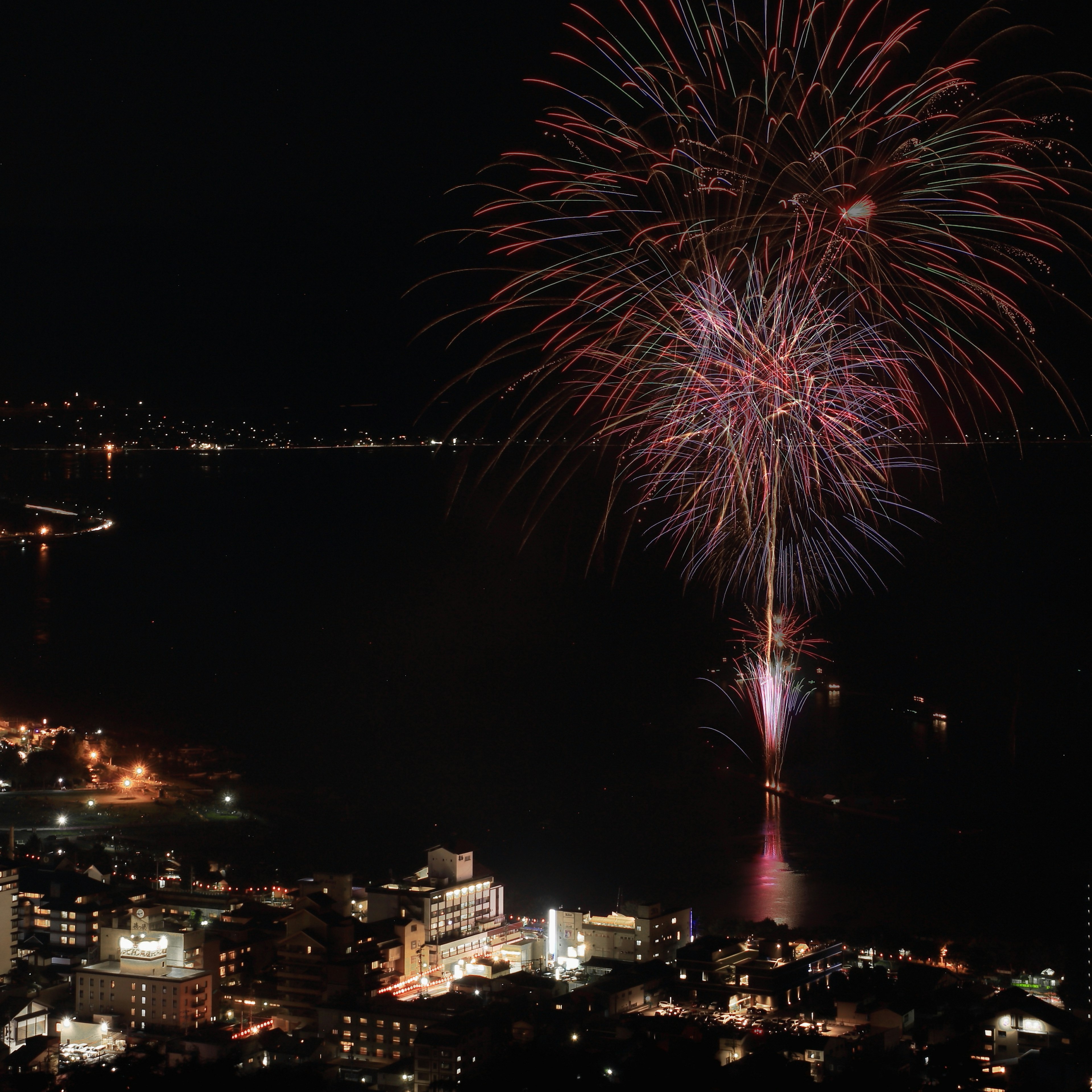 Fuochi d'artificio che esplodono nel cielo notturno sopra una città costiera