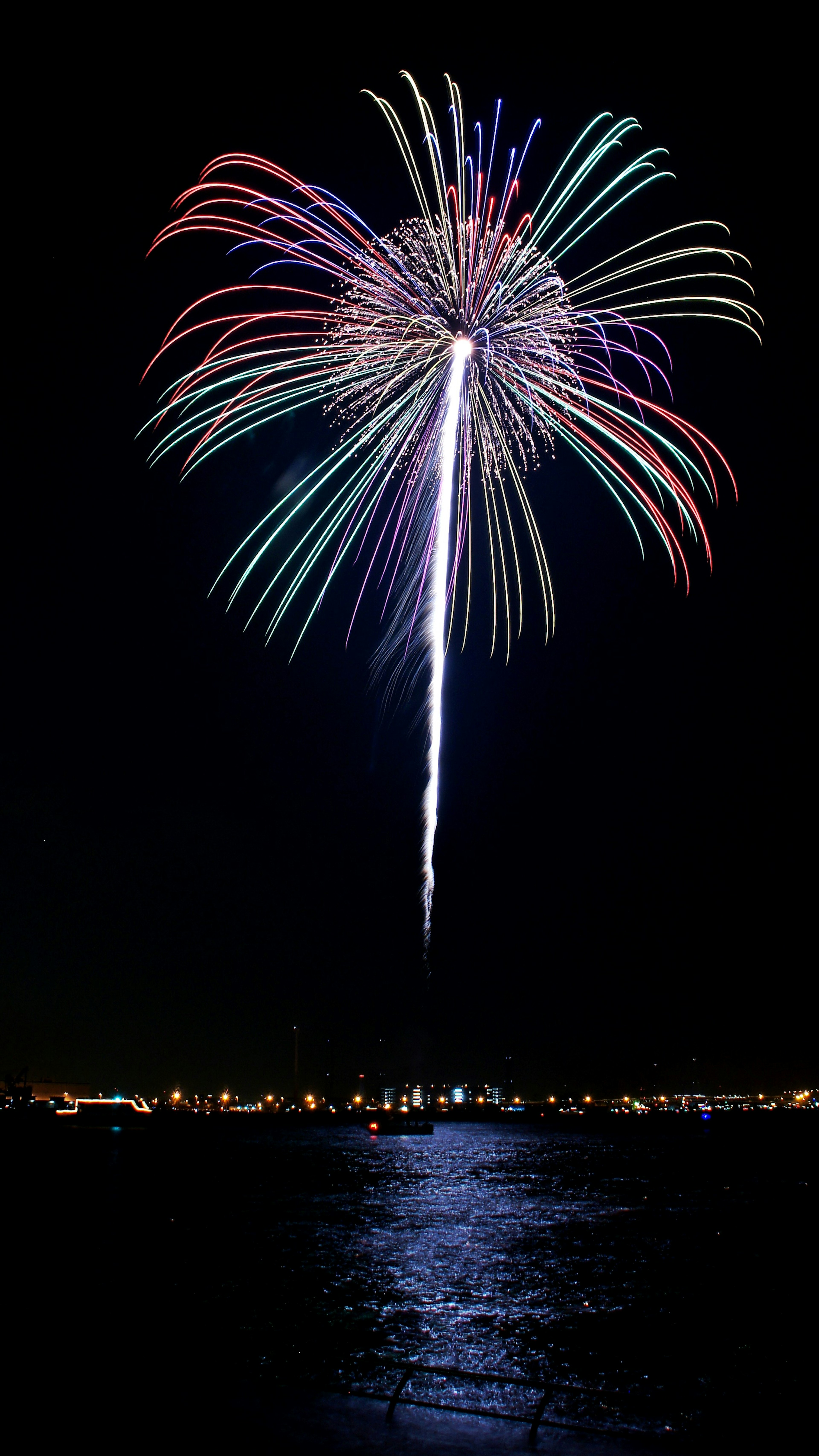 Fuochi d'artificio colorati che esplodono nel cielo notturno riflettendosi sull'acqua