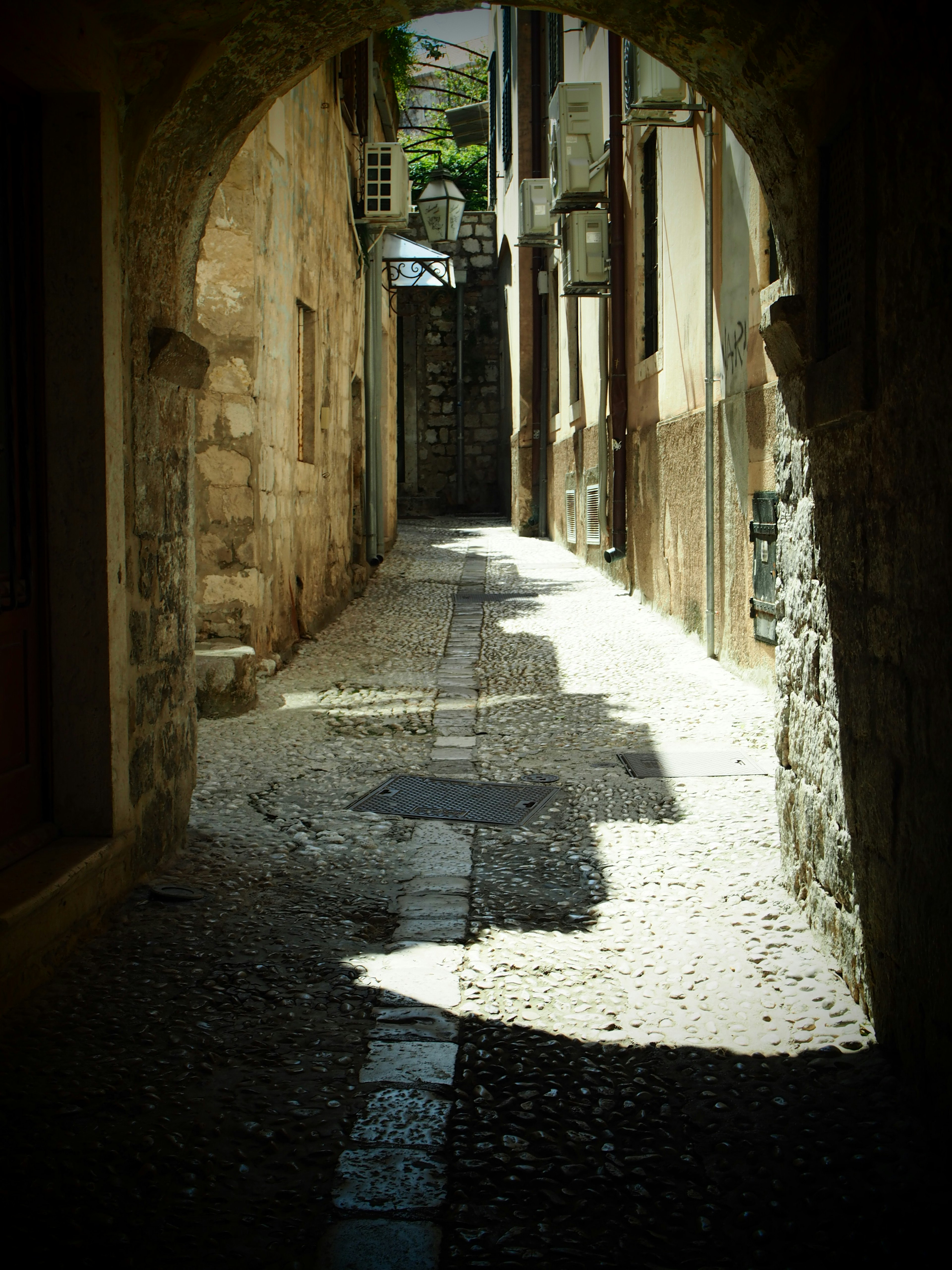 Callejón estrecho de adoquines visible a través de un arco en un pueblo antiguo