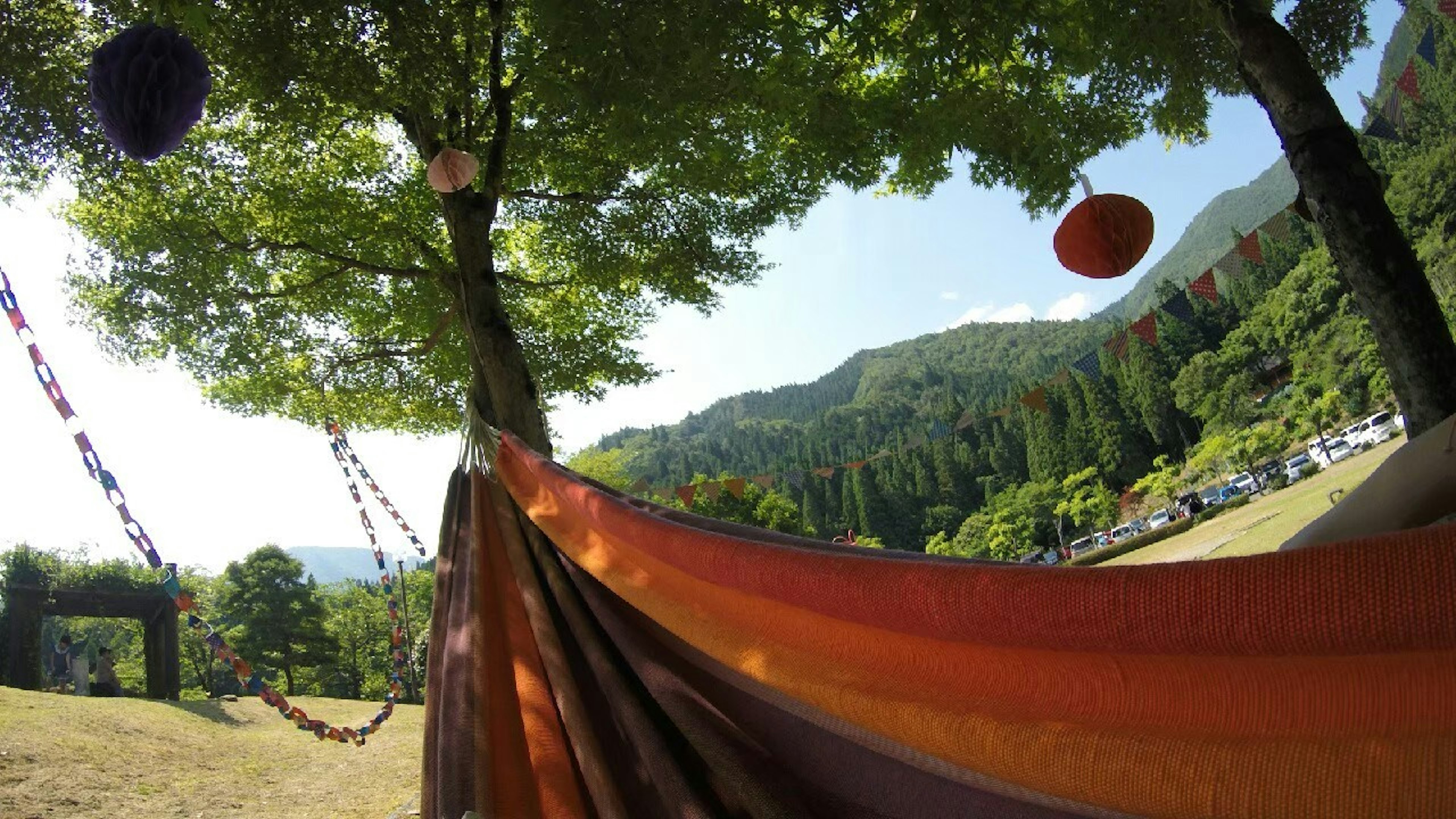 緑の木の下にぶら下がるオレンジ色のハンモックと山の風景