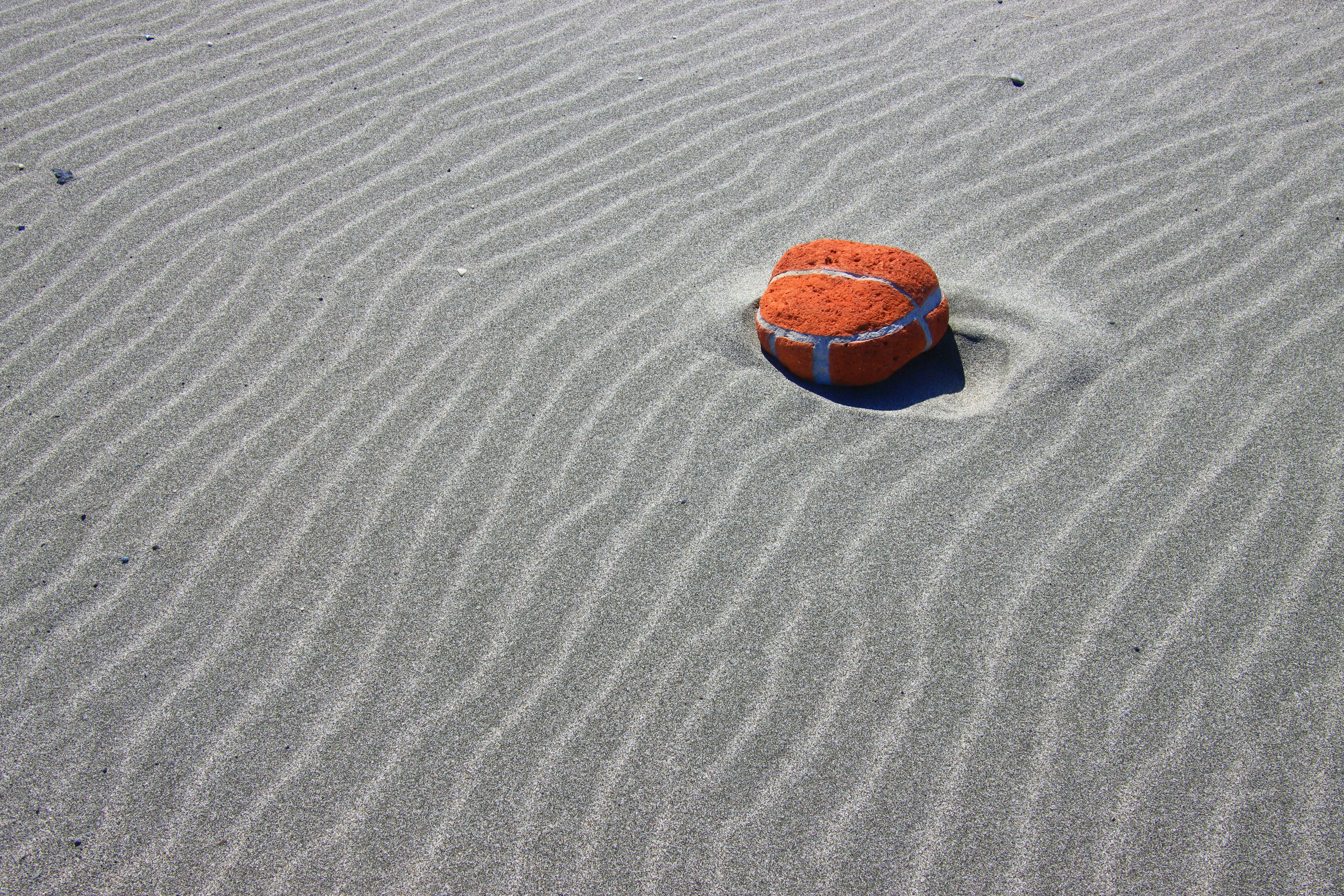 An orange ball resting on a sandy surface with wave-like patterns