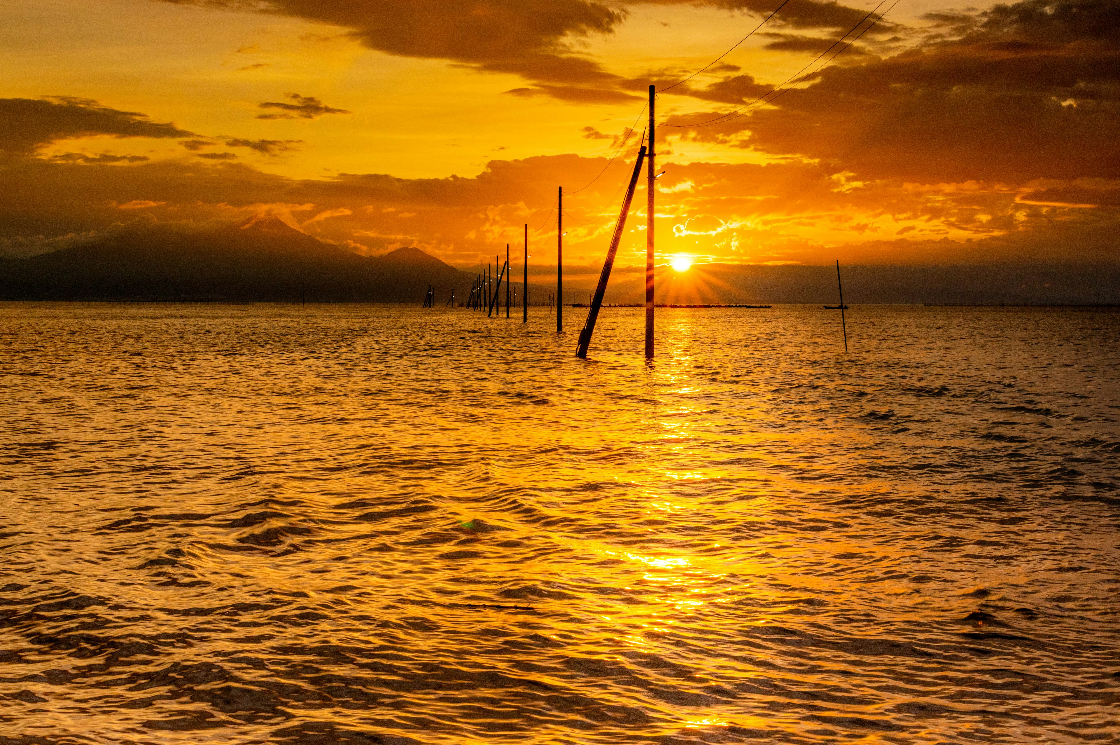 Bellissimo tramonto sul mare con riflessi dorati sull'acqua e pali in silhouette