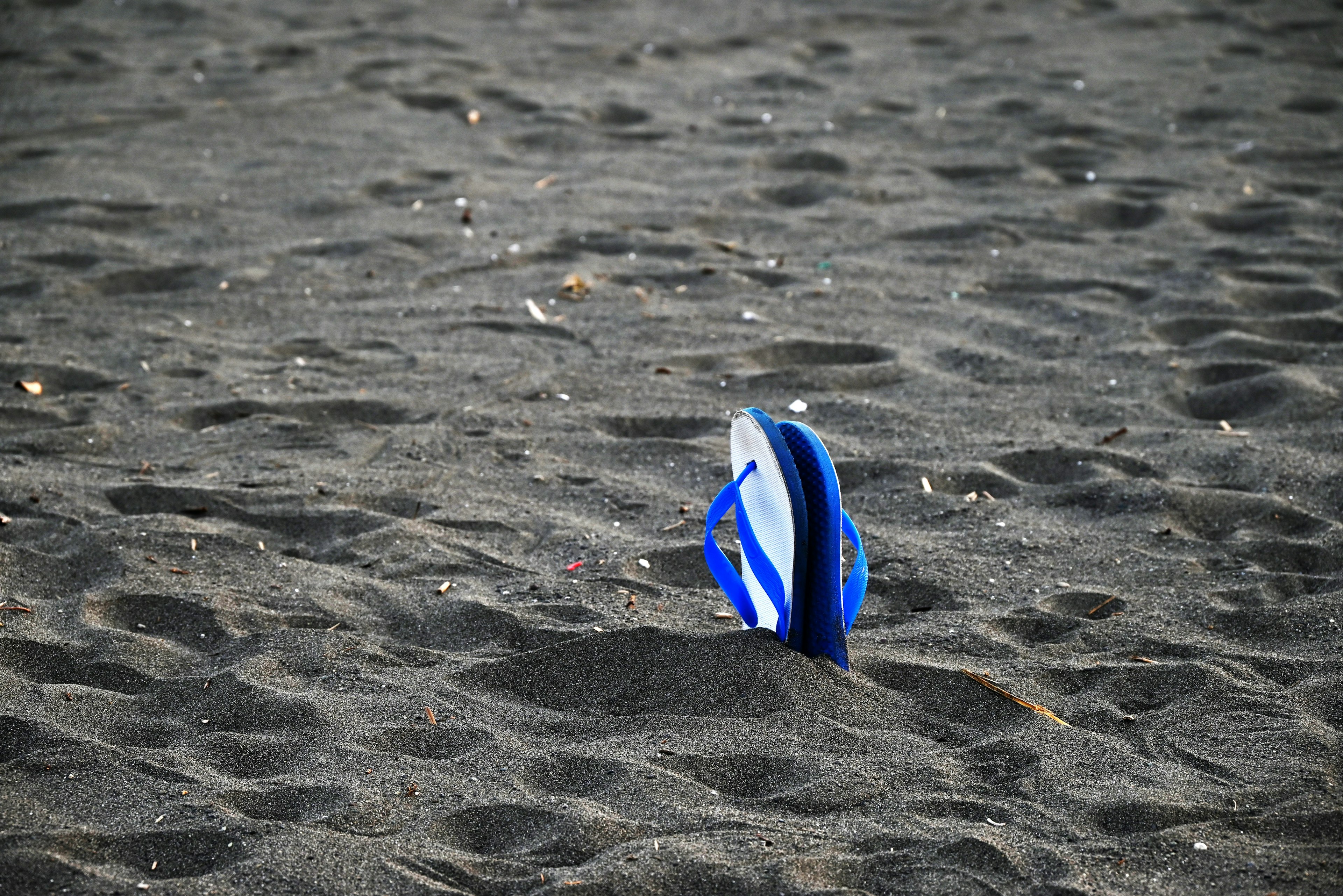 Chancla azul parcialmente enterrada en una playa de arena negra