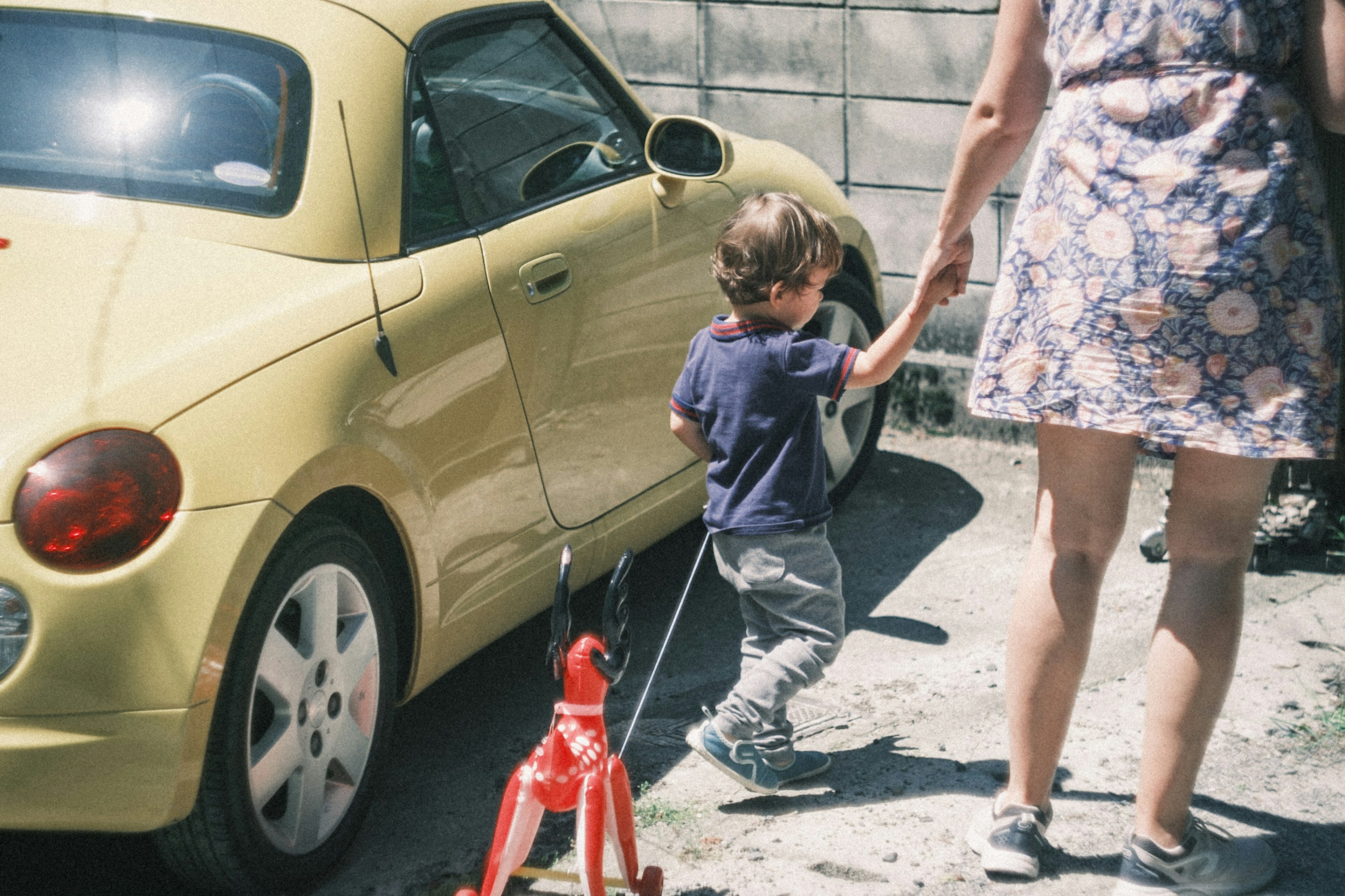 Child holding hands with an adult next to a yellow car