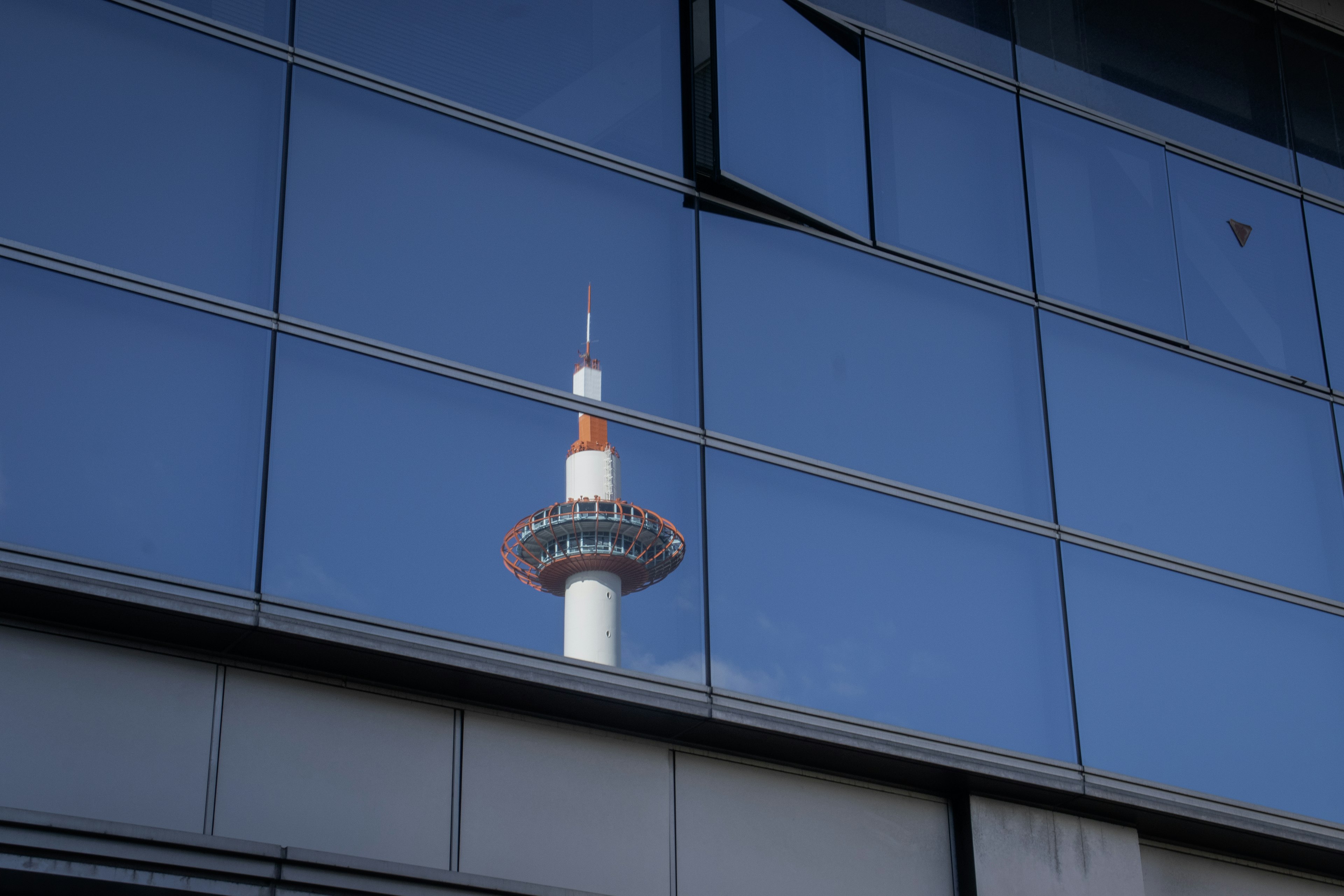 Refleksi Menara Kyoto di kaca gedung dengan langit biru