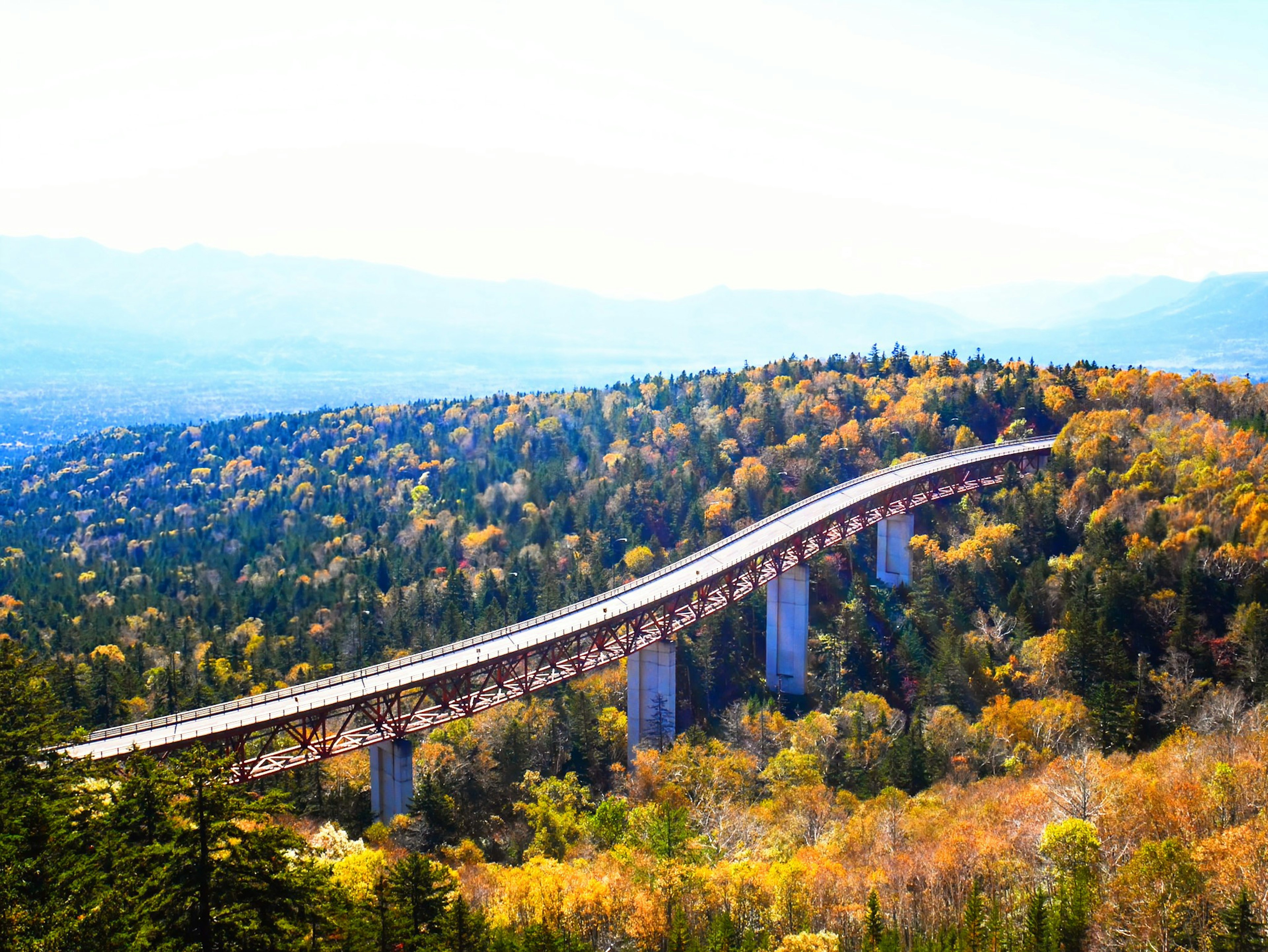 秋の色合いの山々の中に曲がりくねった鉄道橋