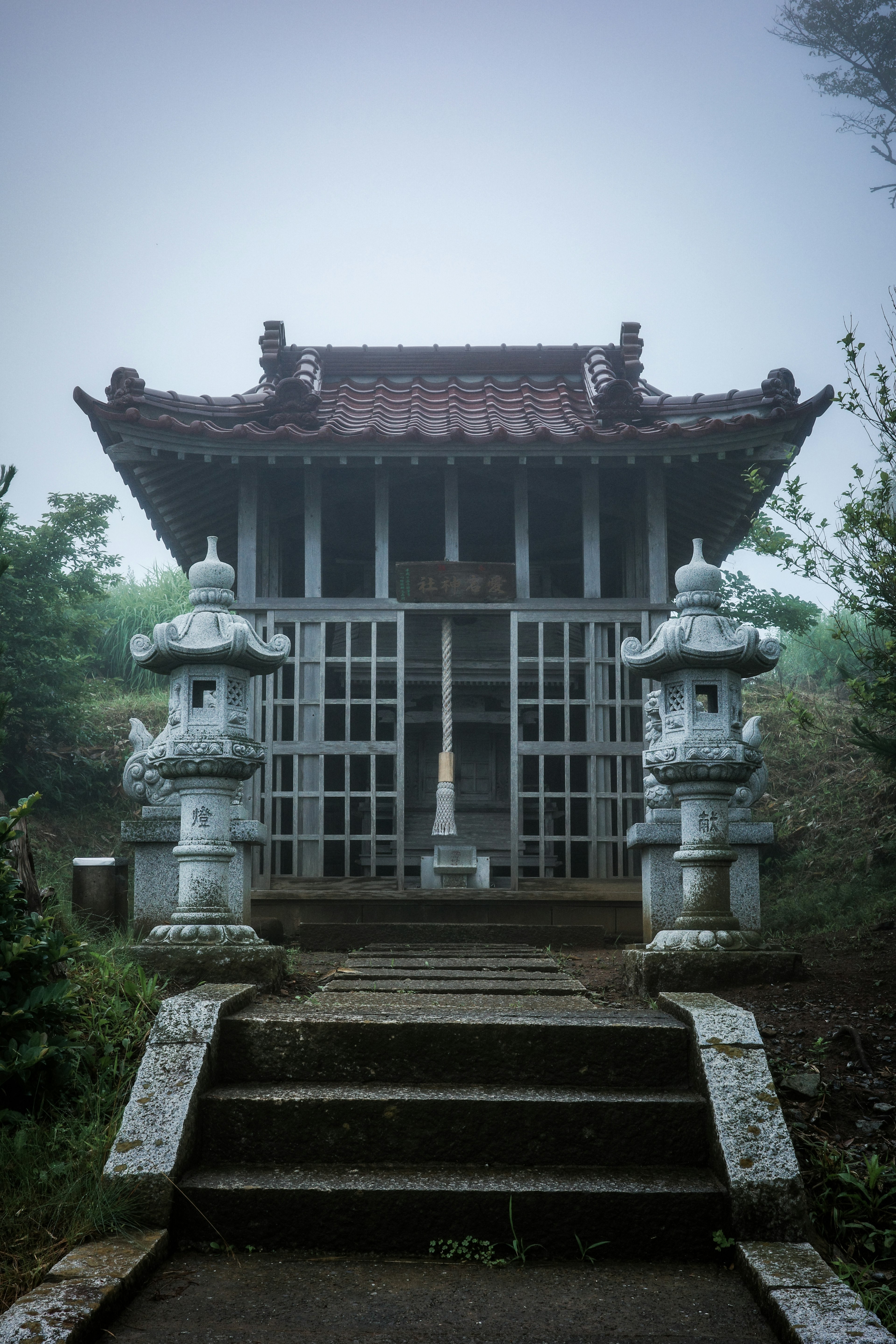 霧の中に佇む古い神社の建物と石灯篭