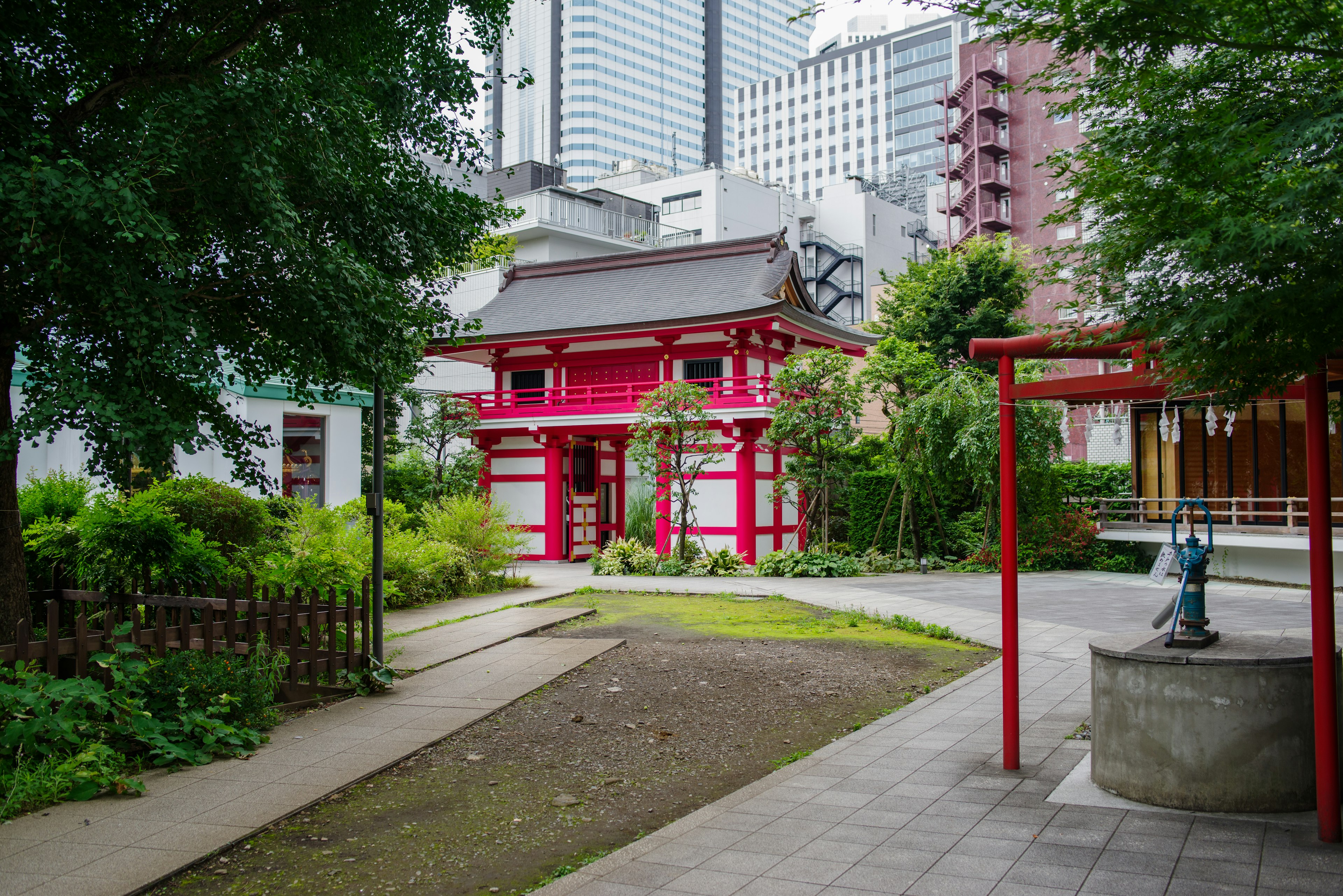 Red shrine gate surrounded by greenery with modern buildings in the background