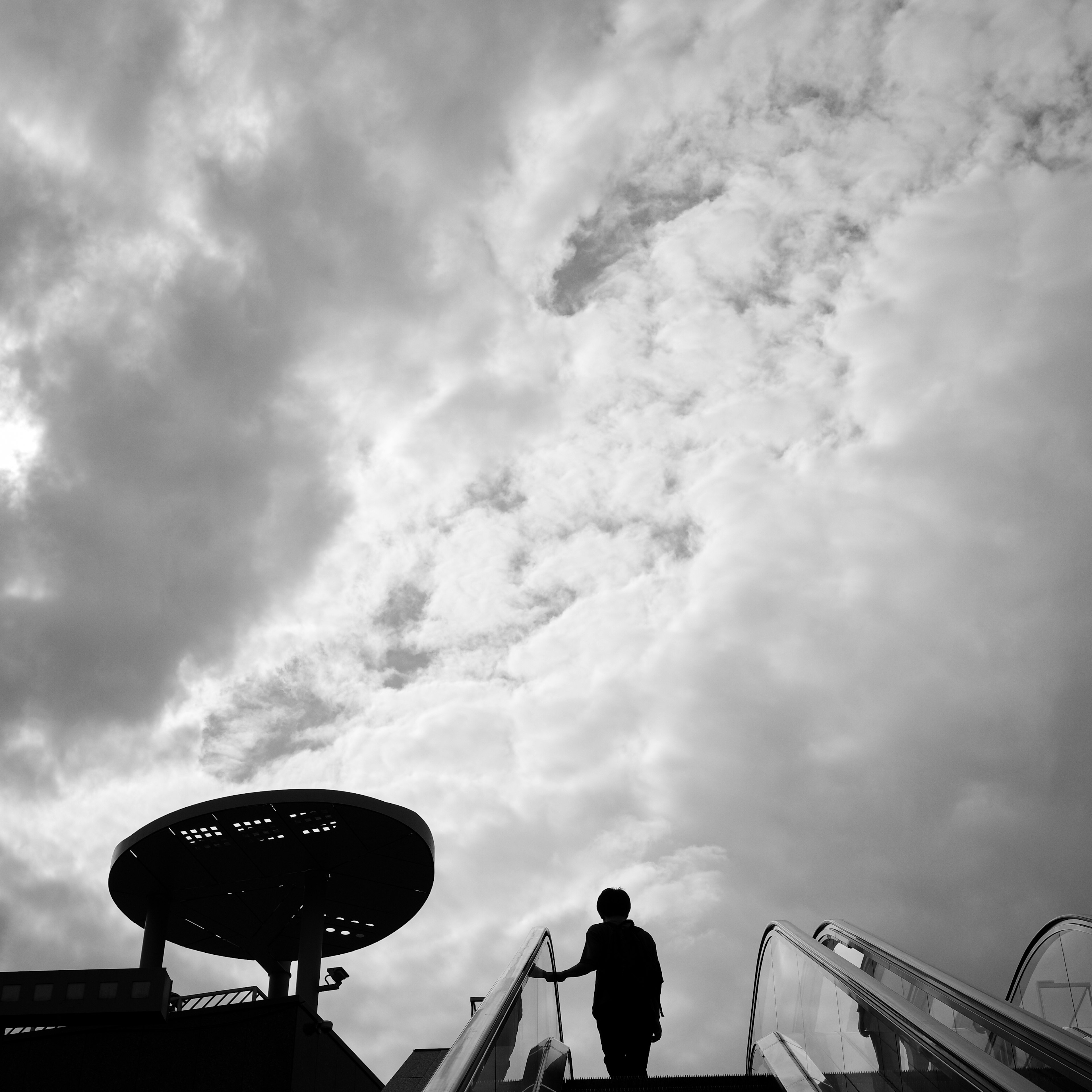 Silhouette d'une personne montant un escalator sous un ciel nuageux