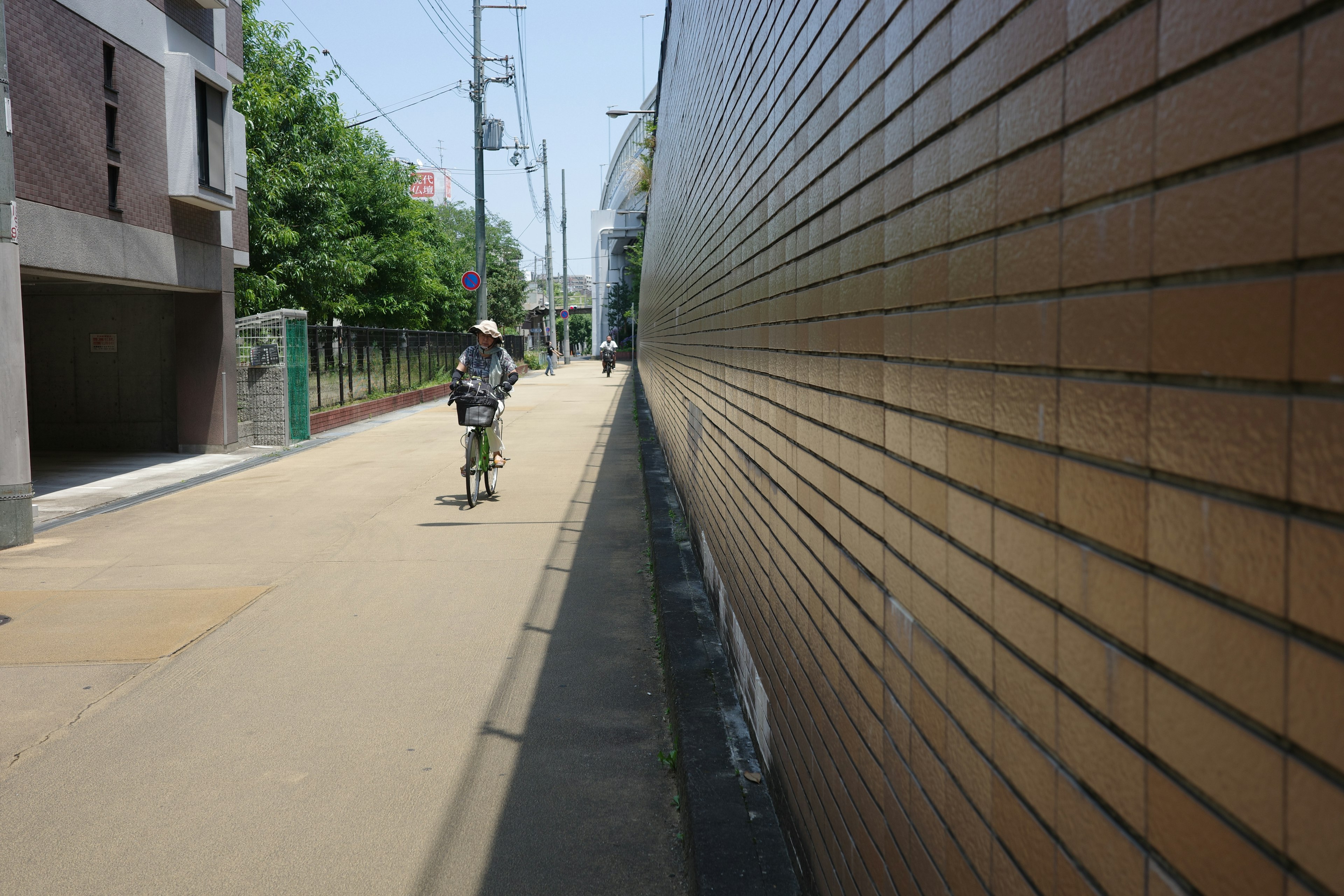 Städtische Szene mit einer Person auf einem Fahrrad, einer Ziegelmauer auf der linken Seite und Bäumen entlang der Straße auf der rechten Seite