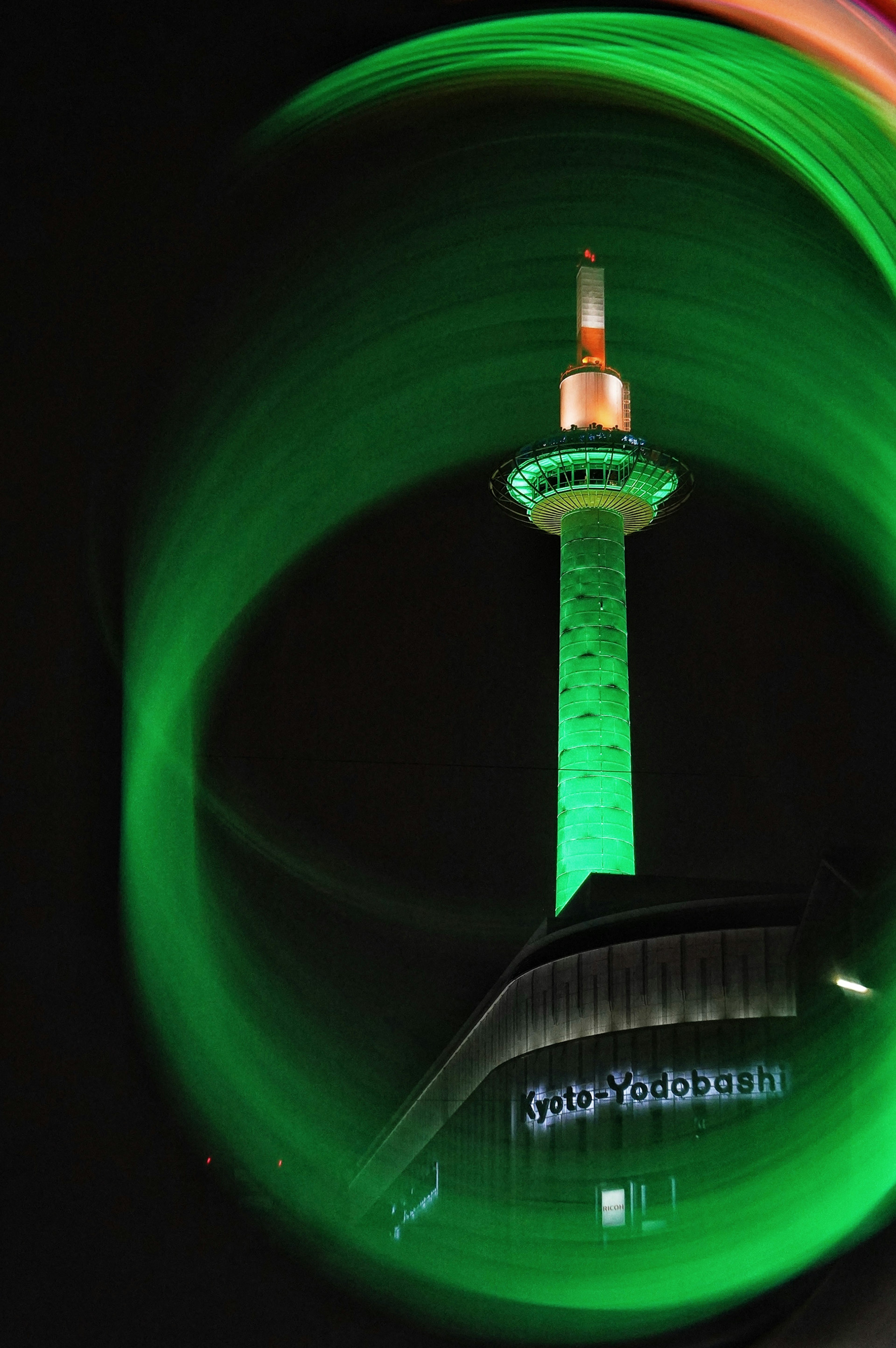 Vista nocturna de la Torre de Tokio iluminada en verde con efectos de luz en espiral