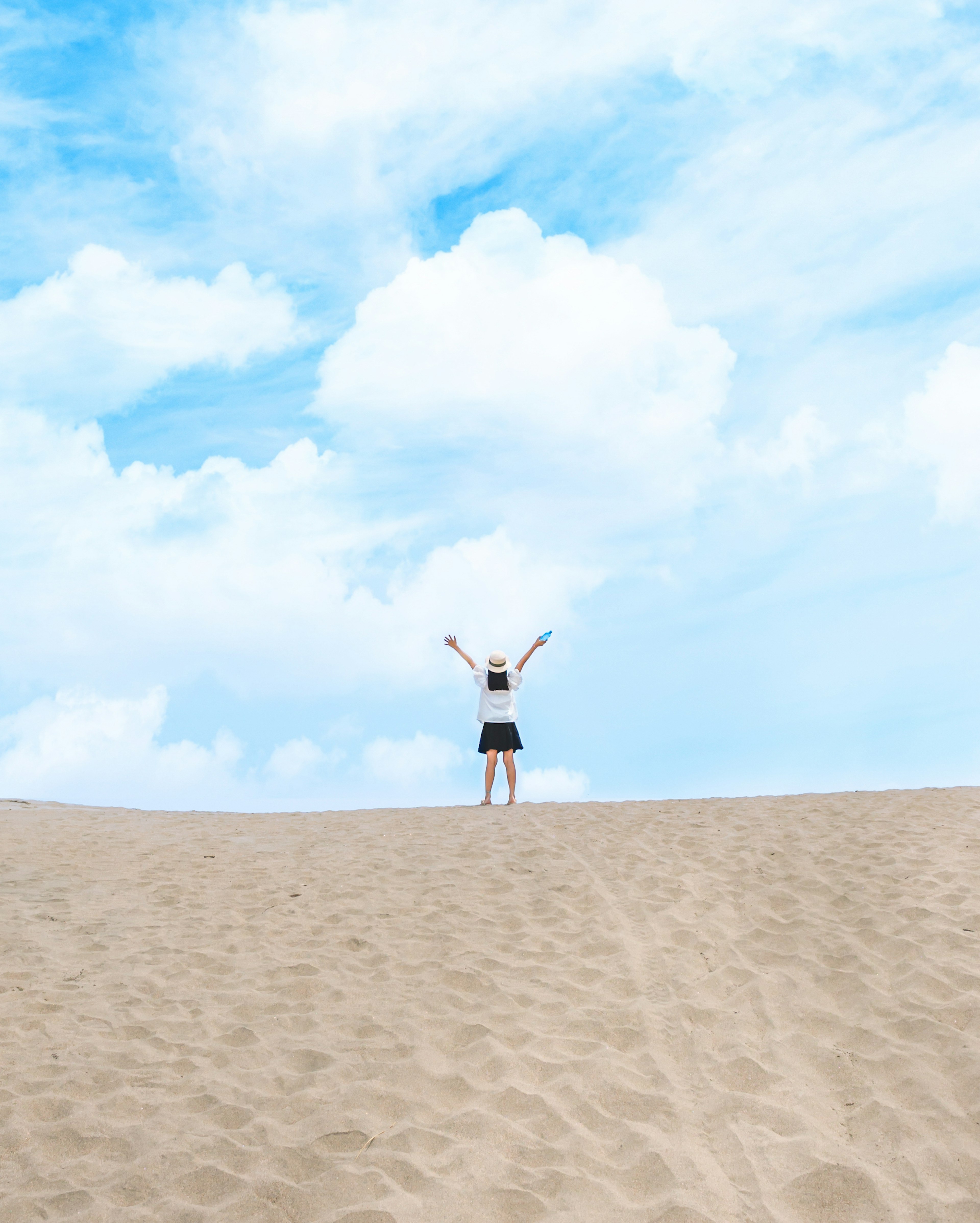 Person standing on sand dune with arms raised under a blue sky