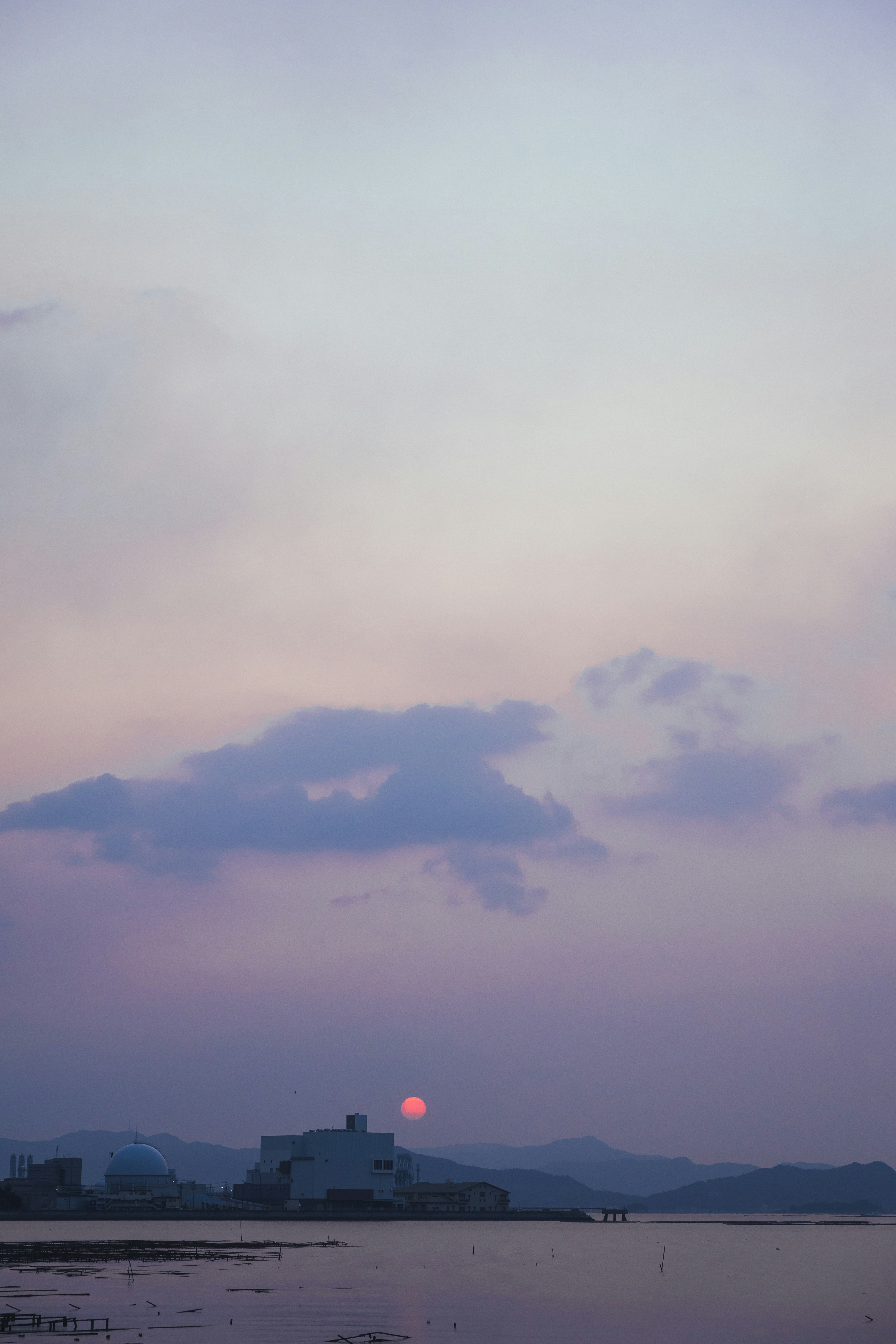 Ciel au coucher de soleil avec des nuages et un soleil rouge reflété sur l'eau