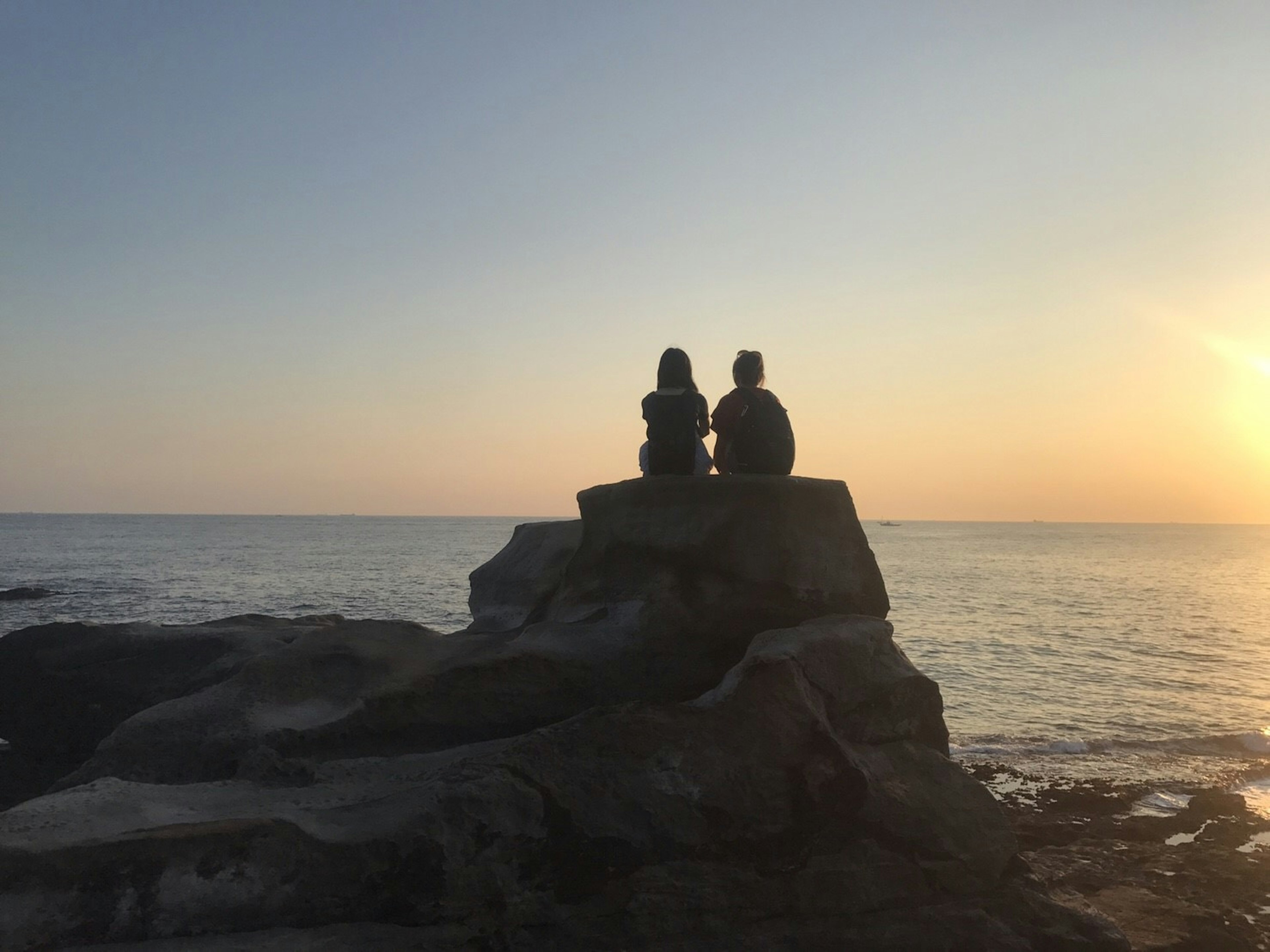 Silhouette of two people sitting on a rock against a sunset