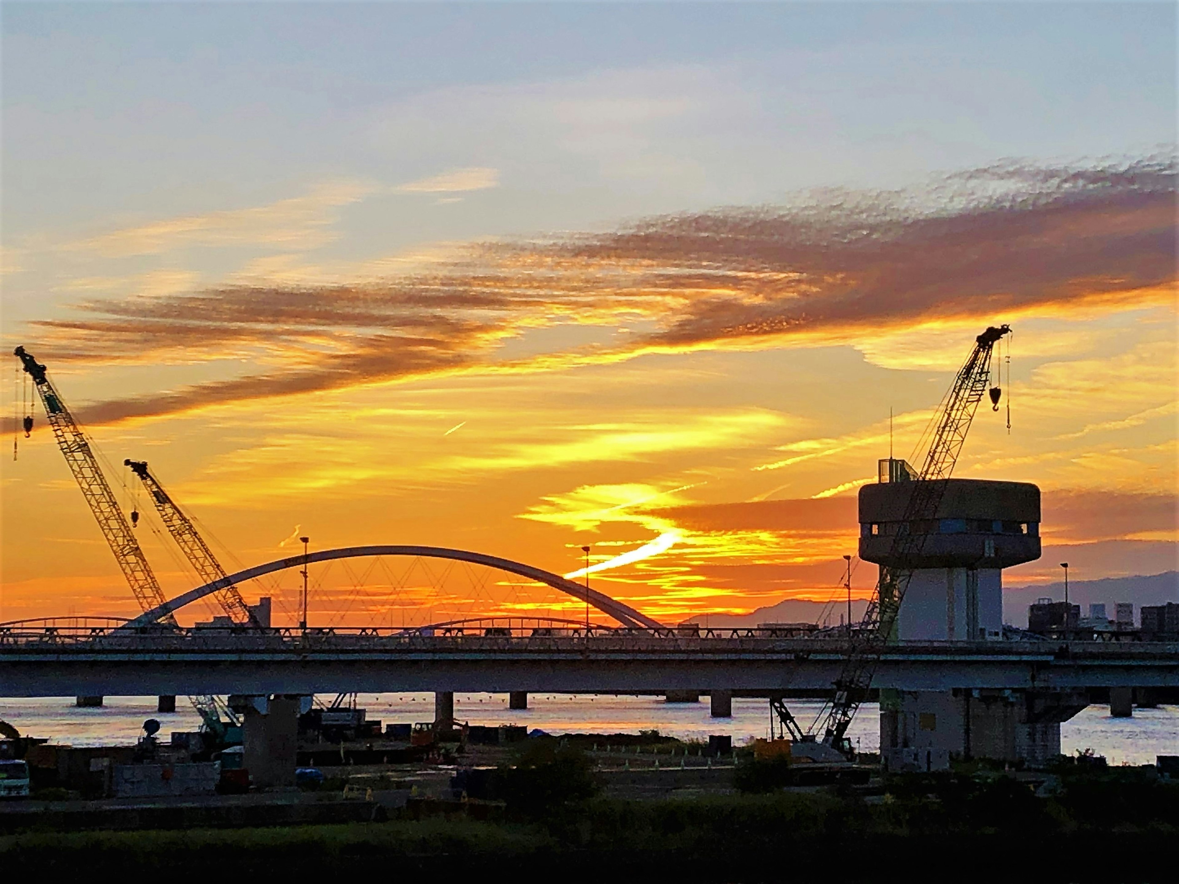 Vista panoramica di un cielo al tramonto con un ponte e gru in silhouette all'orizzonte