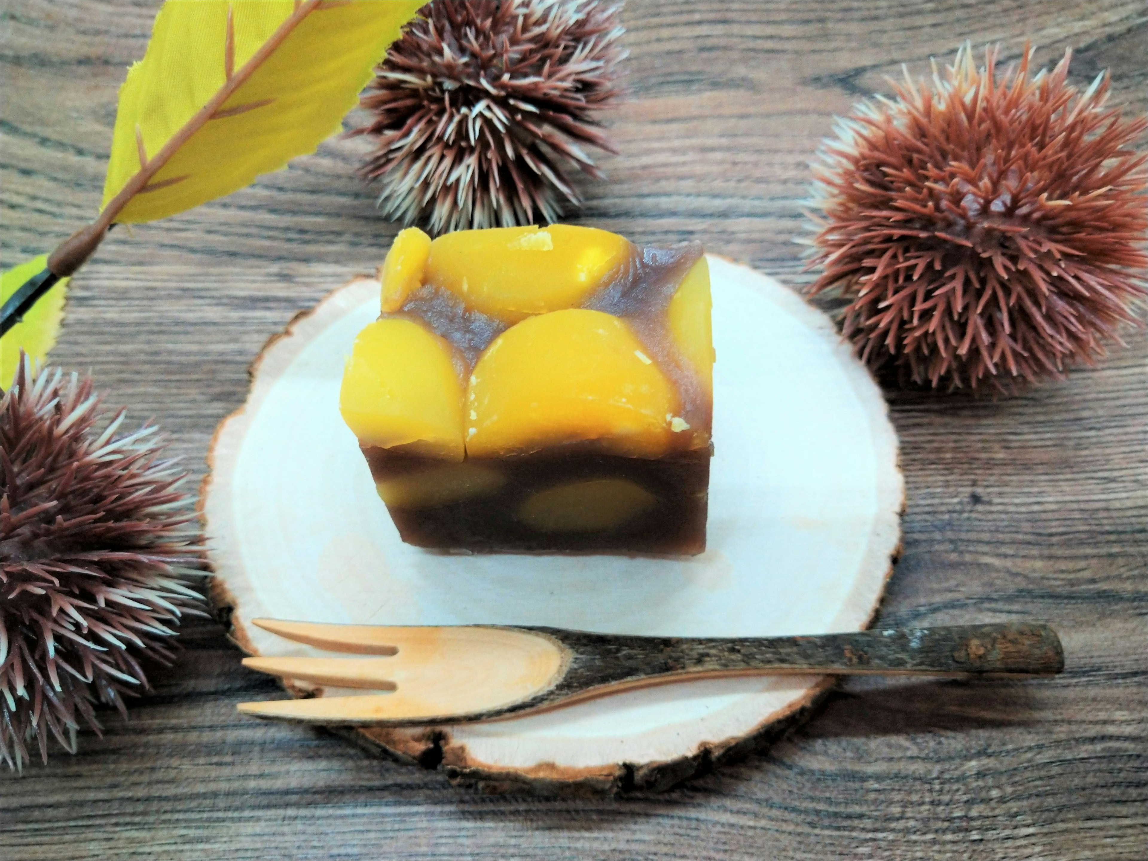 A slice of traditional Japanese dessert on a wooden plate surrounded by chestnuts and autumn leaves