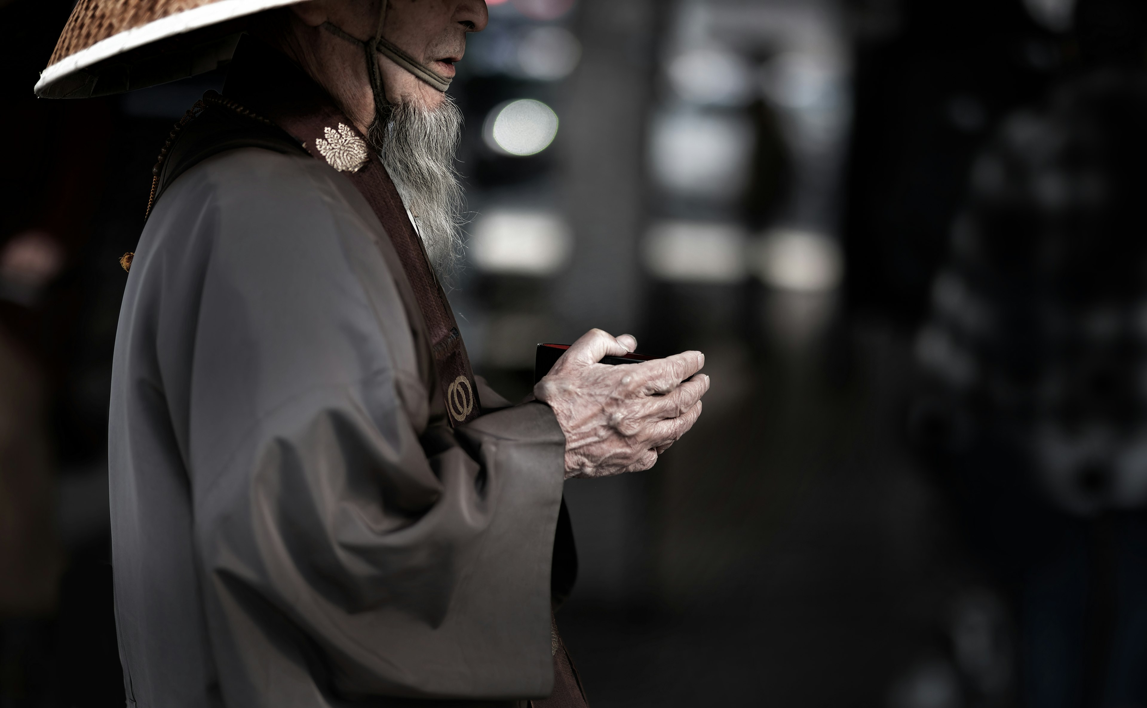 An elderly man wearing a hat is holding his hands together