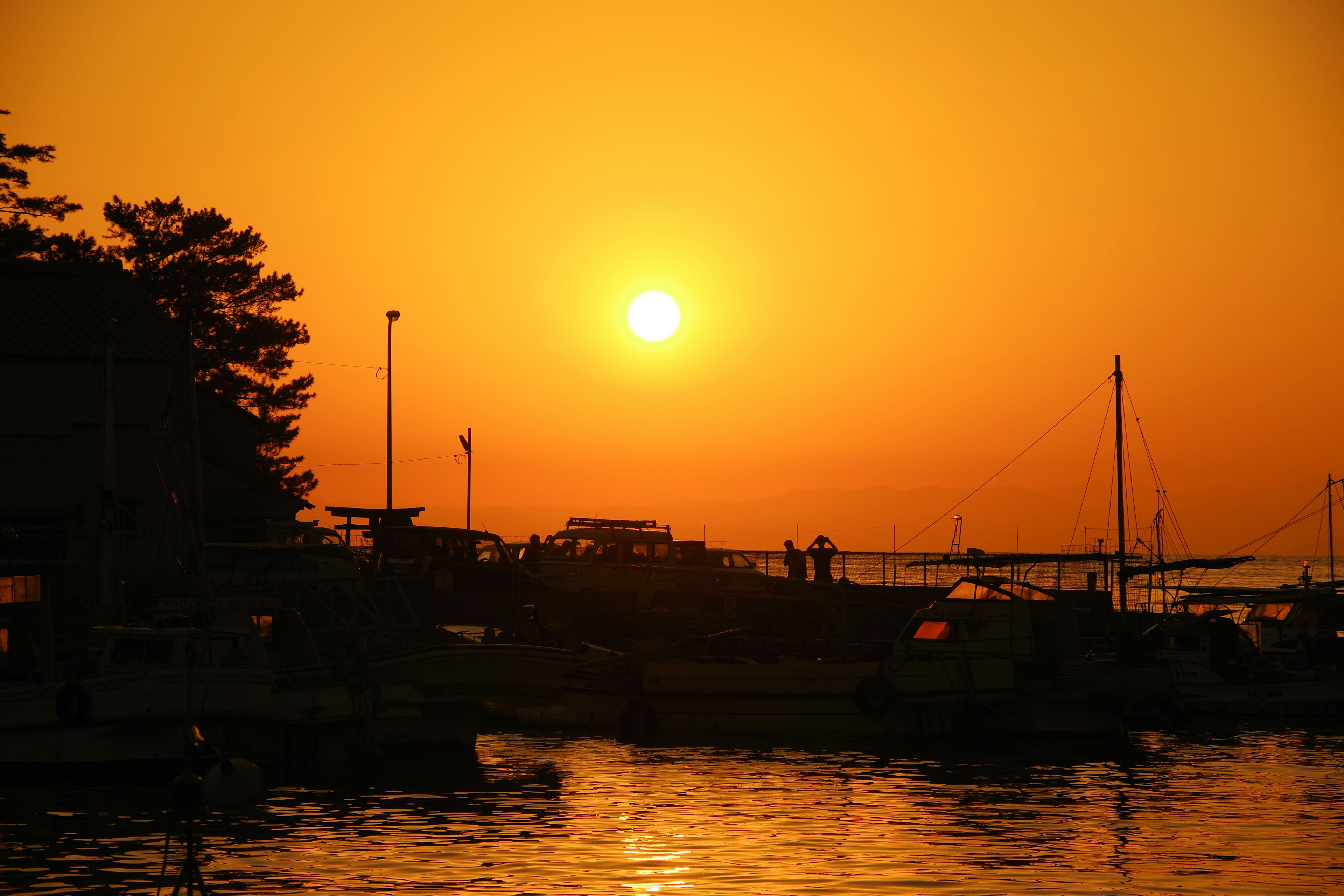 Küsten-Sonnenuntergangsszene mit silhouettierten Booten und Menschen