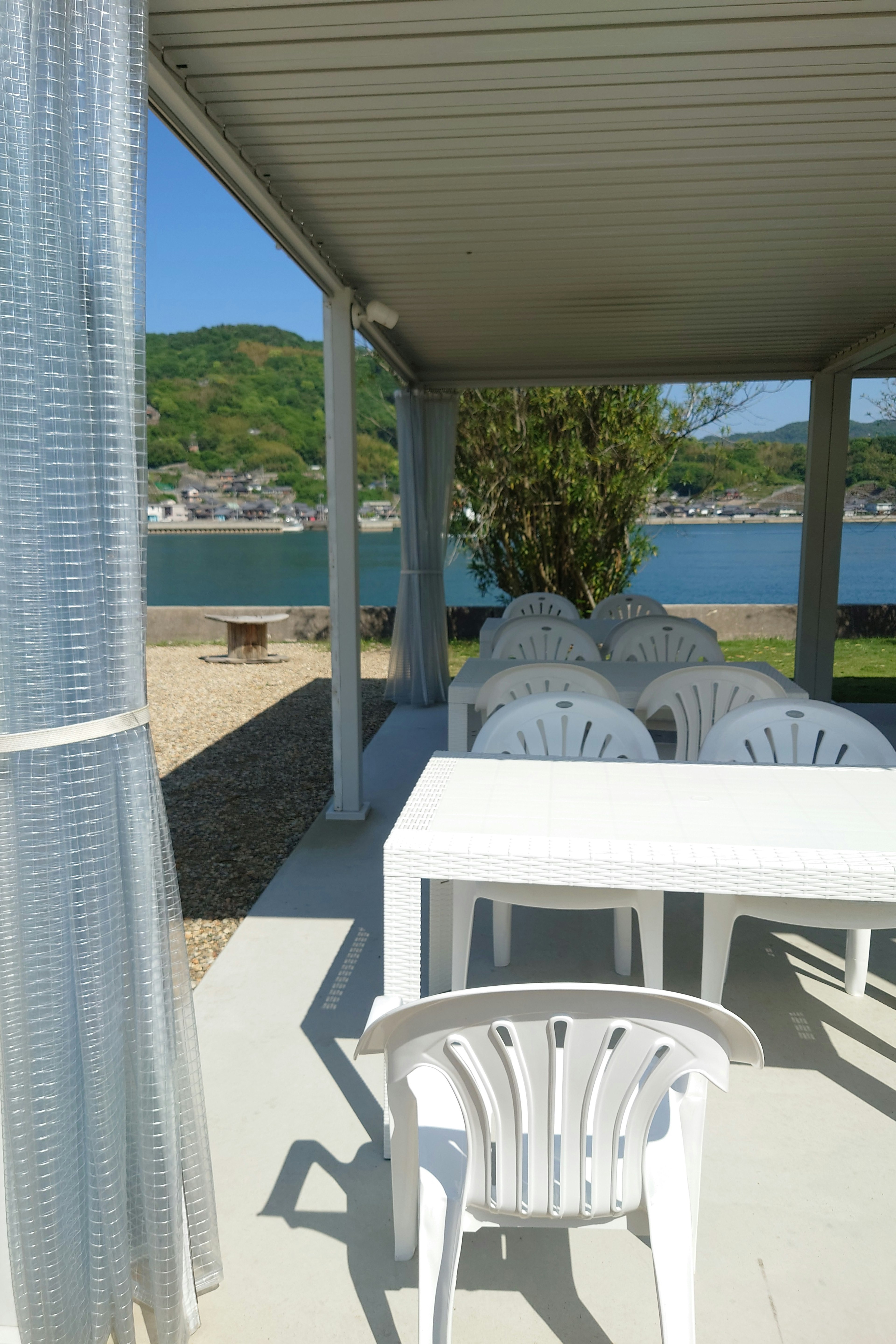 Outdoor pavilion featuring white tables and chairs with a view of green hills and a lake