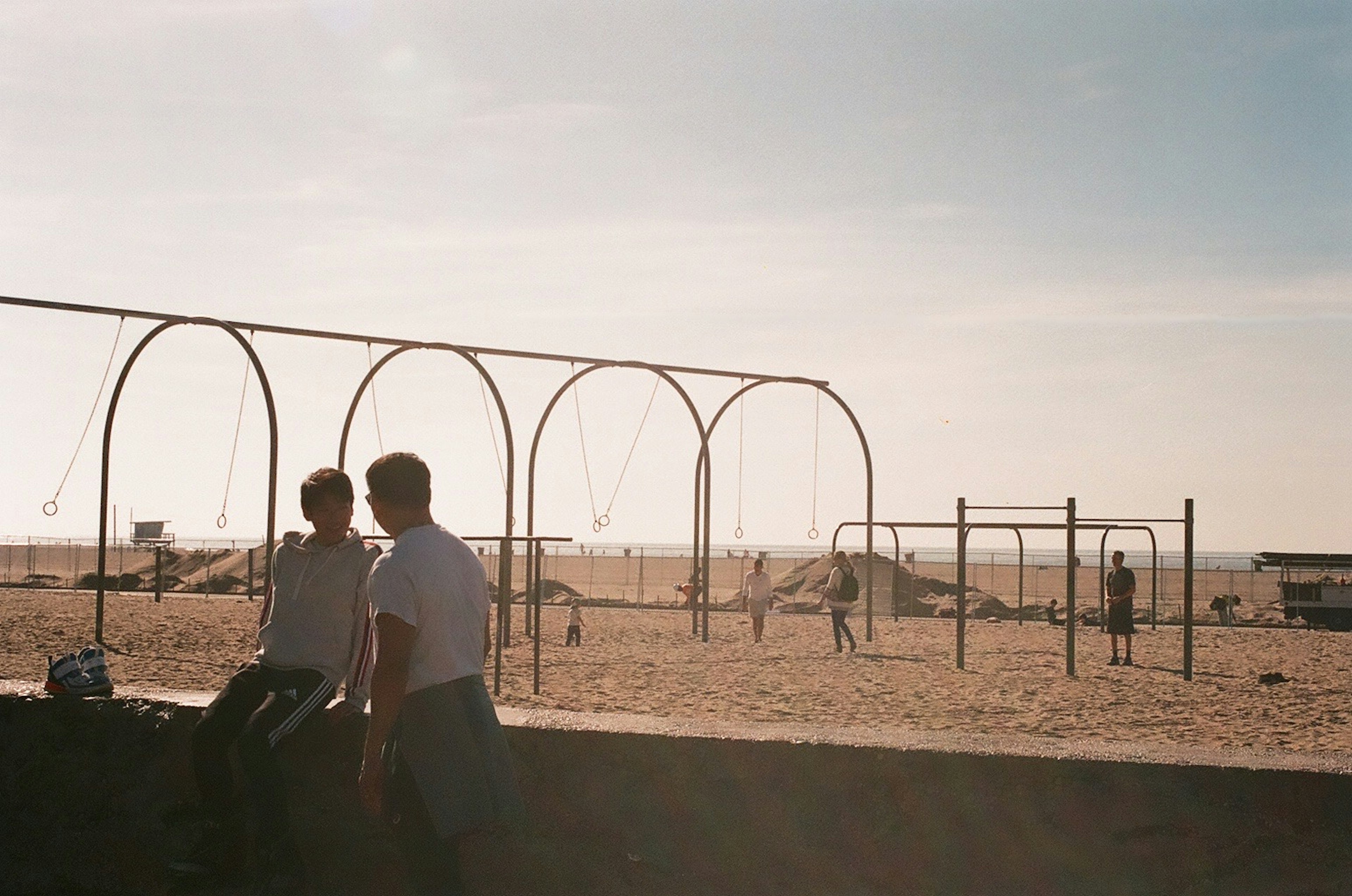 Two people sitting near a playground with swings at the beach