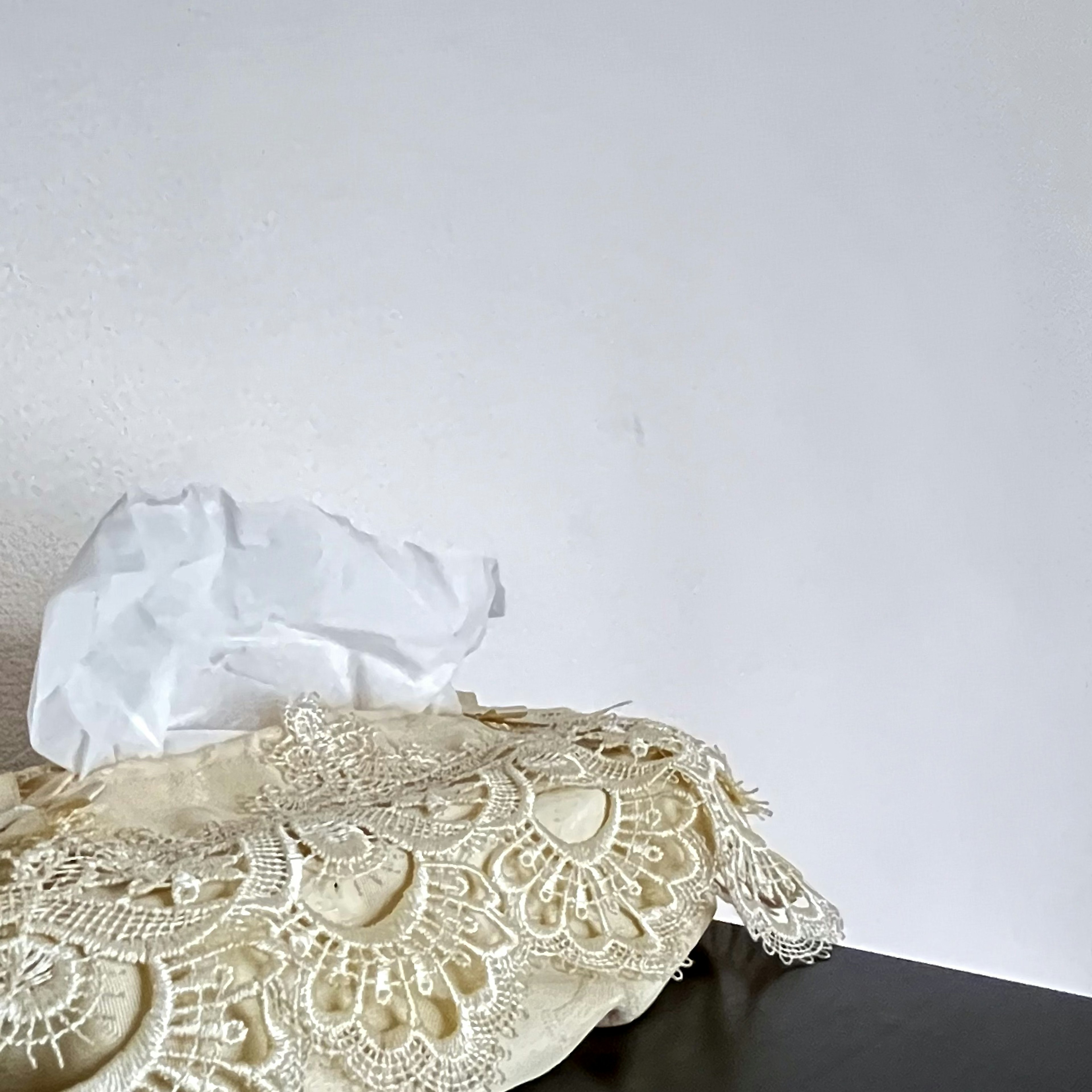 Lace tissue box cover with tissues in front of a white wall