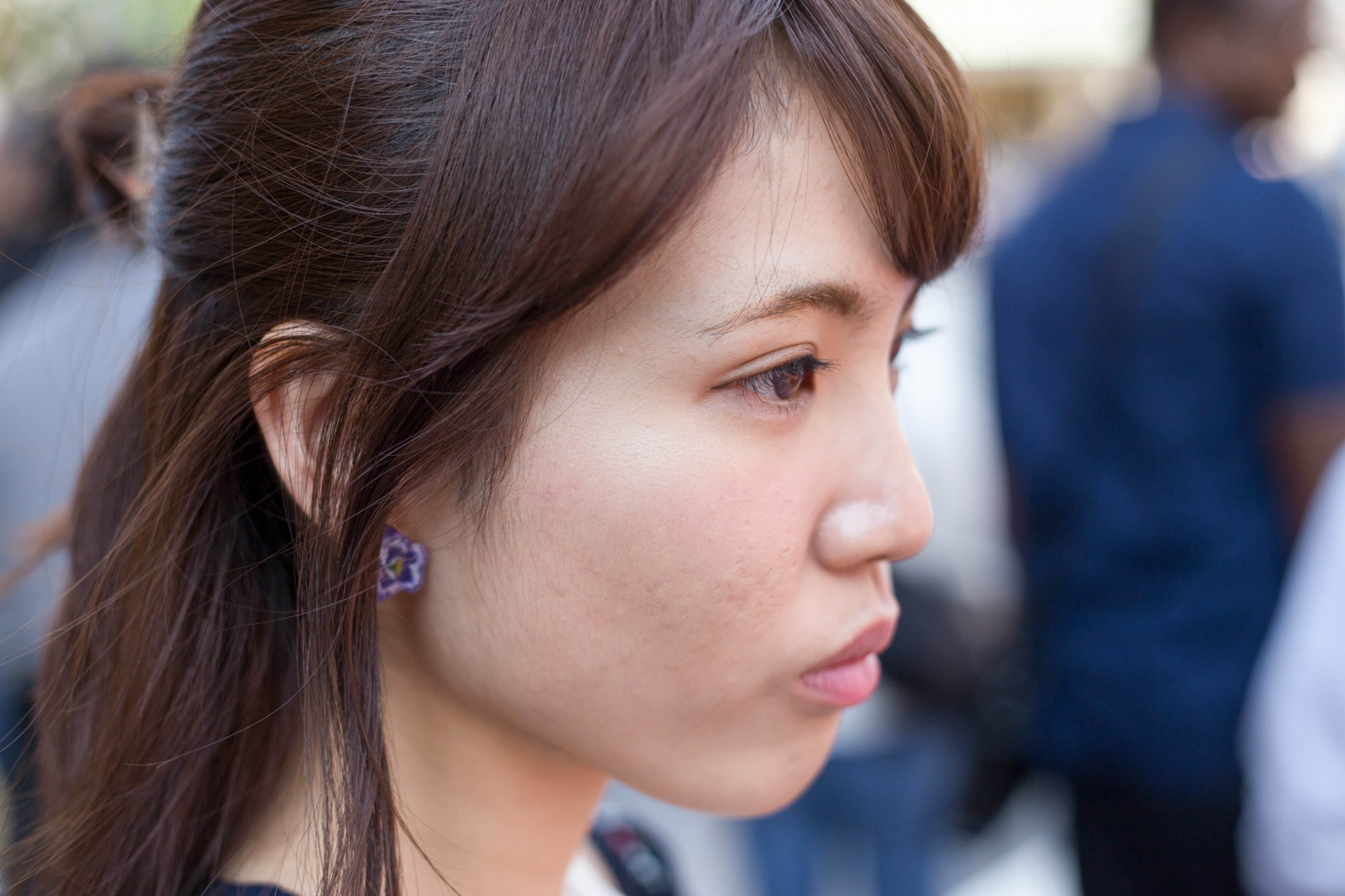 Profile of a woman with brown hair wearing purple earrings background features blurred people