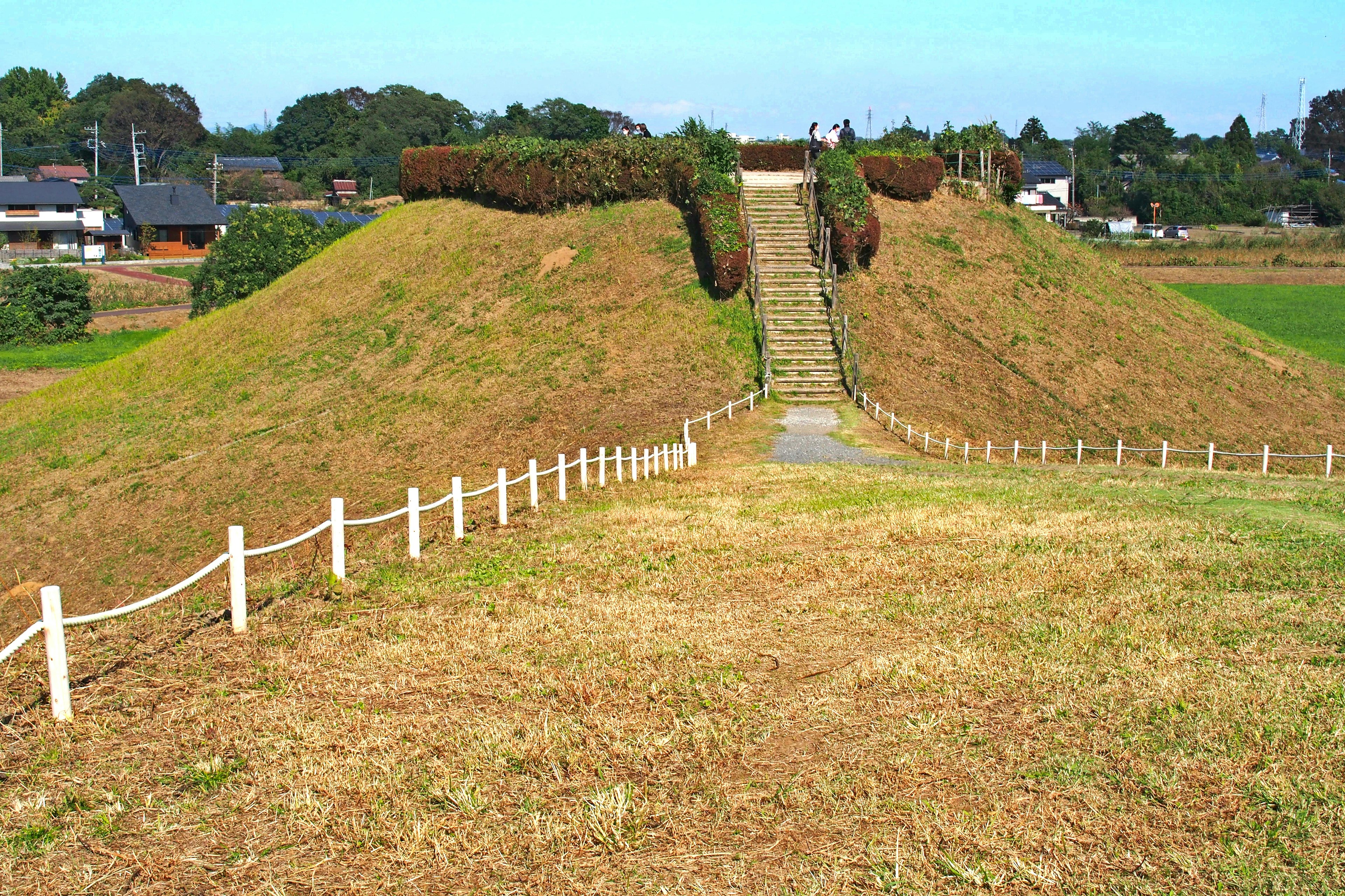 Paisaje con dos montículos que parecen sitios de enterramiento antiguos con una escalera central y campos verdes alrededor