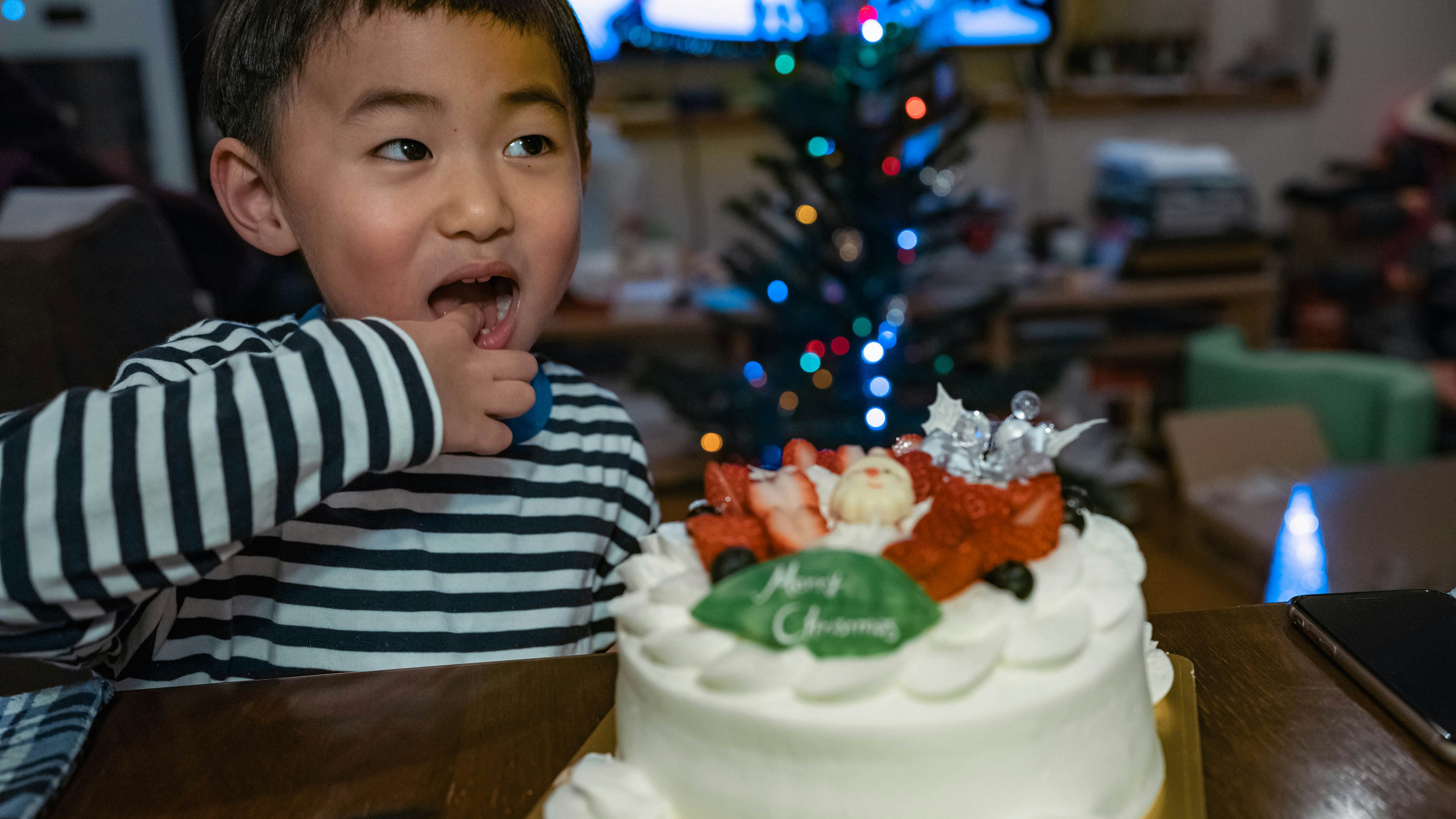 一個孩子在享用聖誕蛋糕，背景有聖誕樹