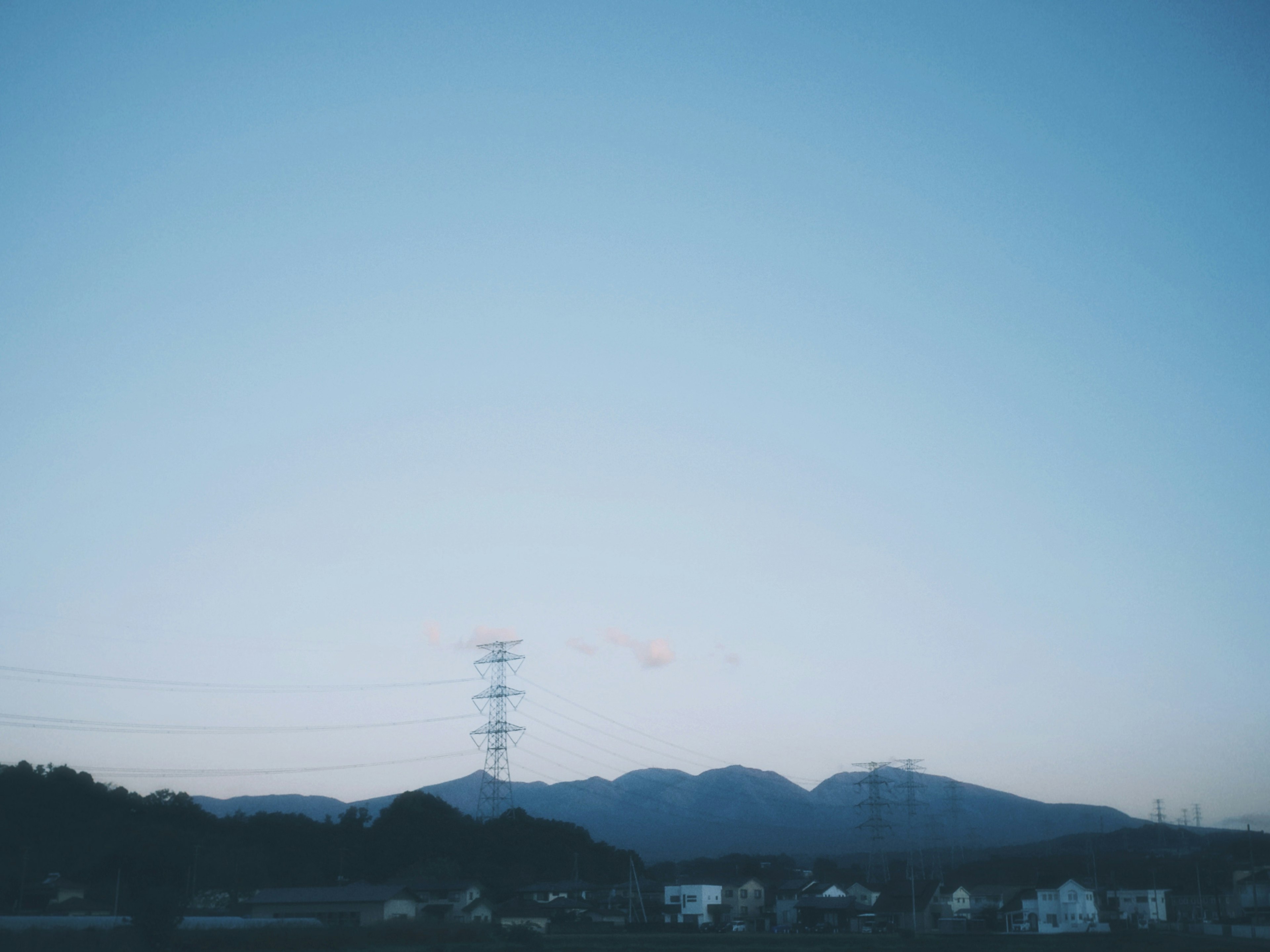 青空の下に広がる山々と電柱が見える風景