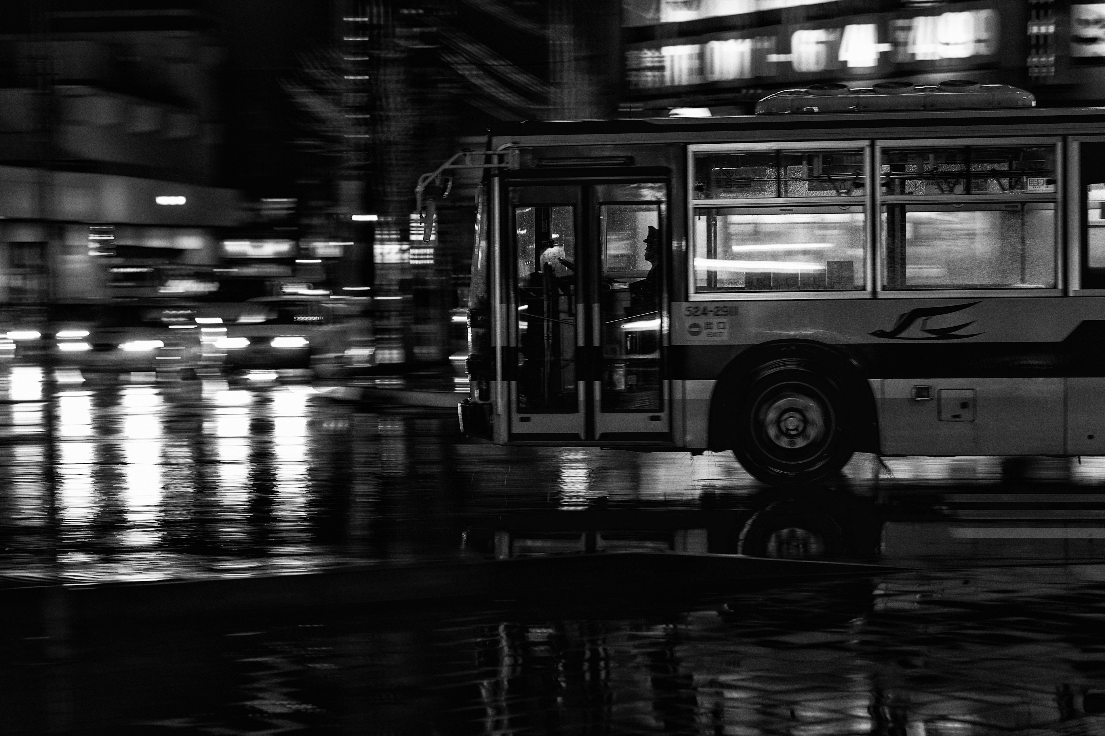 Black and white image of a bus moving through a city at night