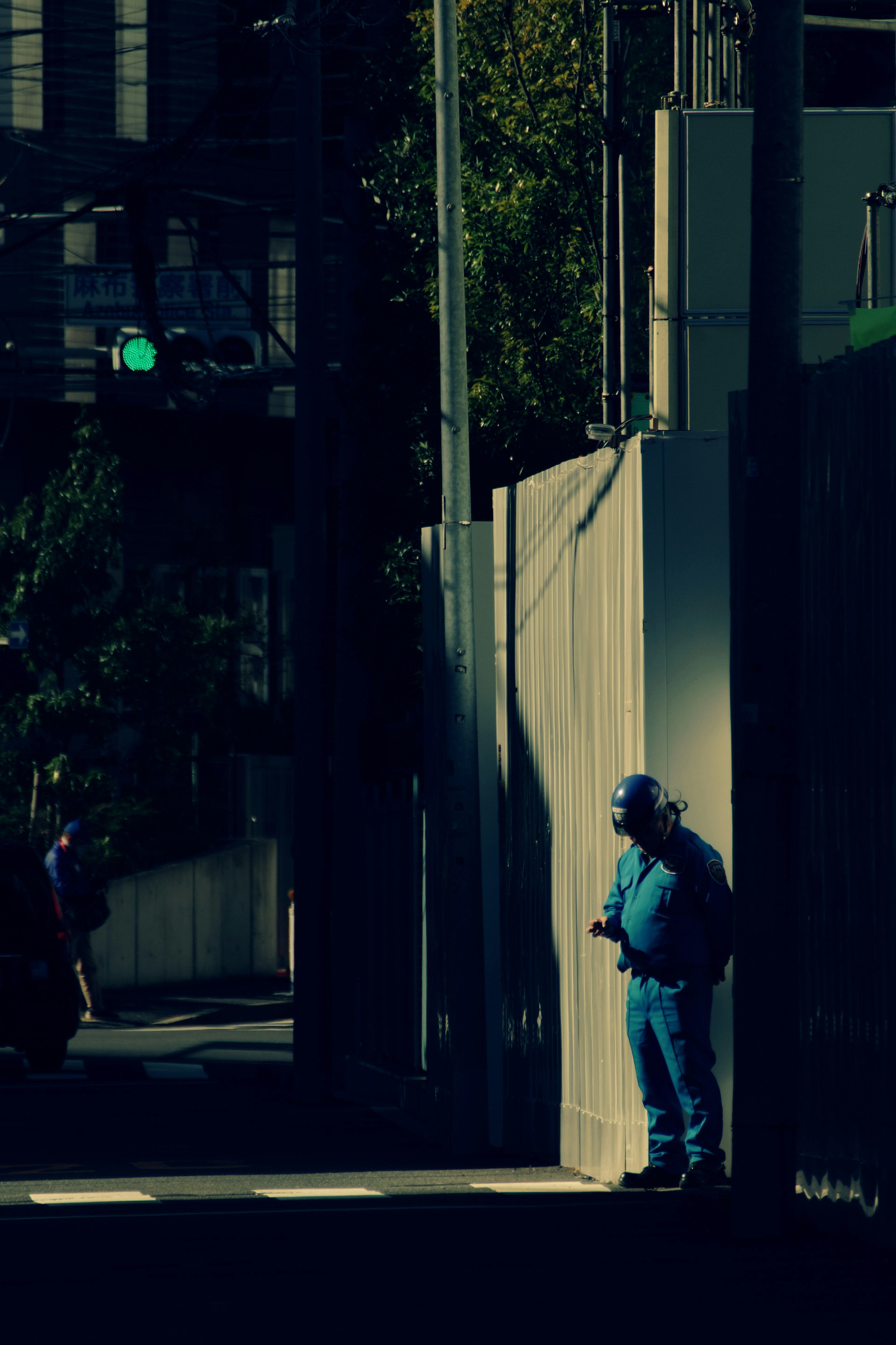 A security guard in a blue uniform leaning against a wall on a street corner